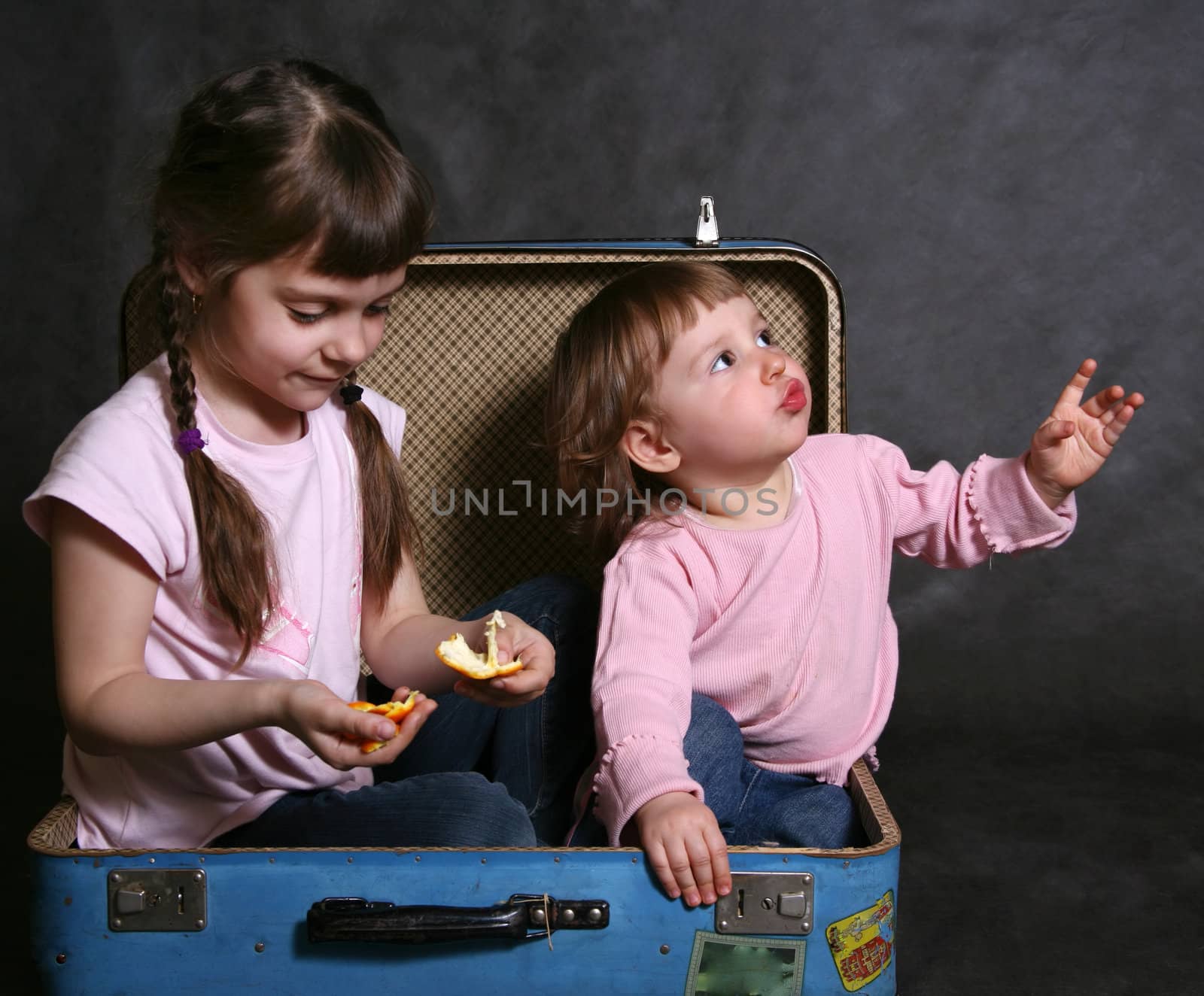 Two sisters sit in a blue suitcase