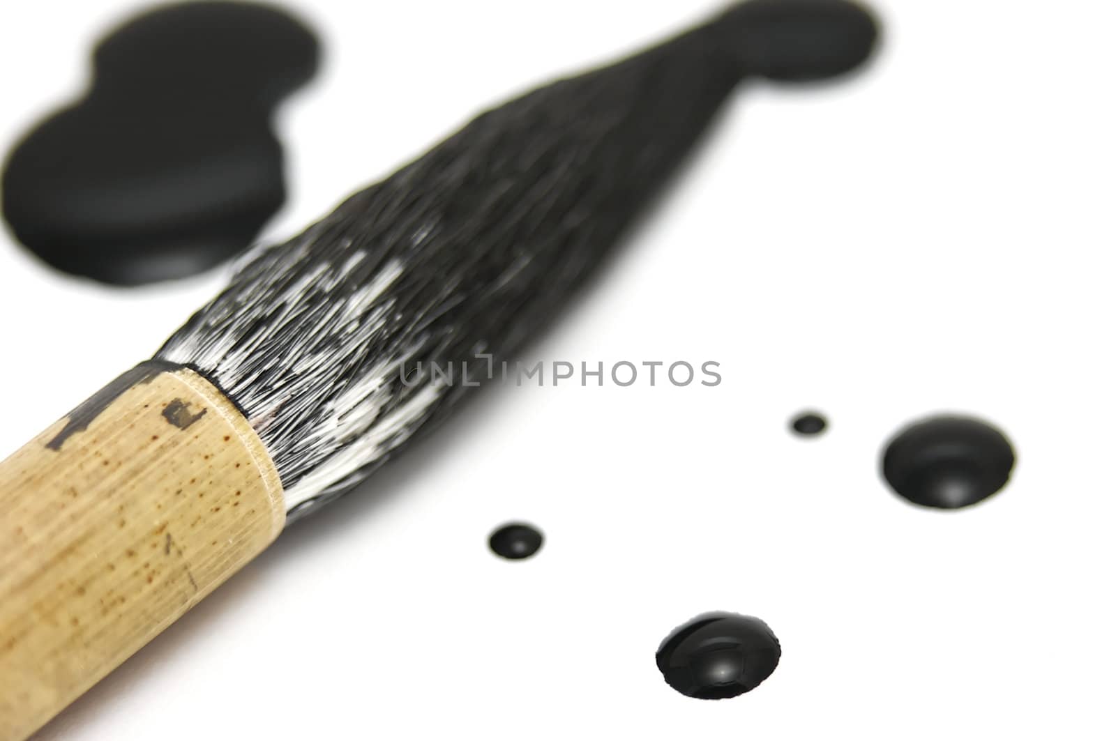 Black chinese ink dots with a calligraphy brush resting nearby. This is a close macro shot with very low depth of field.