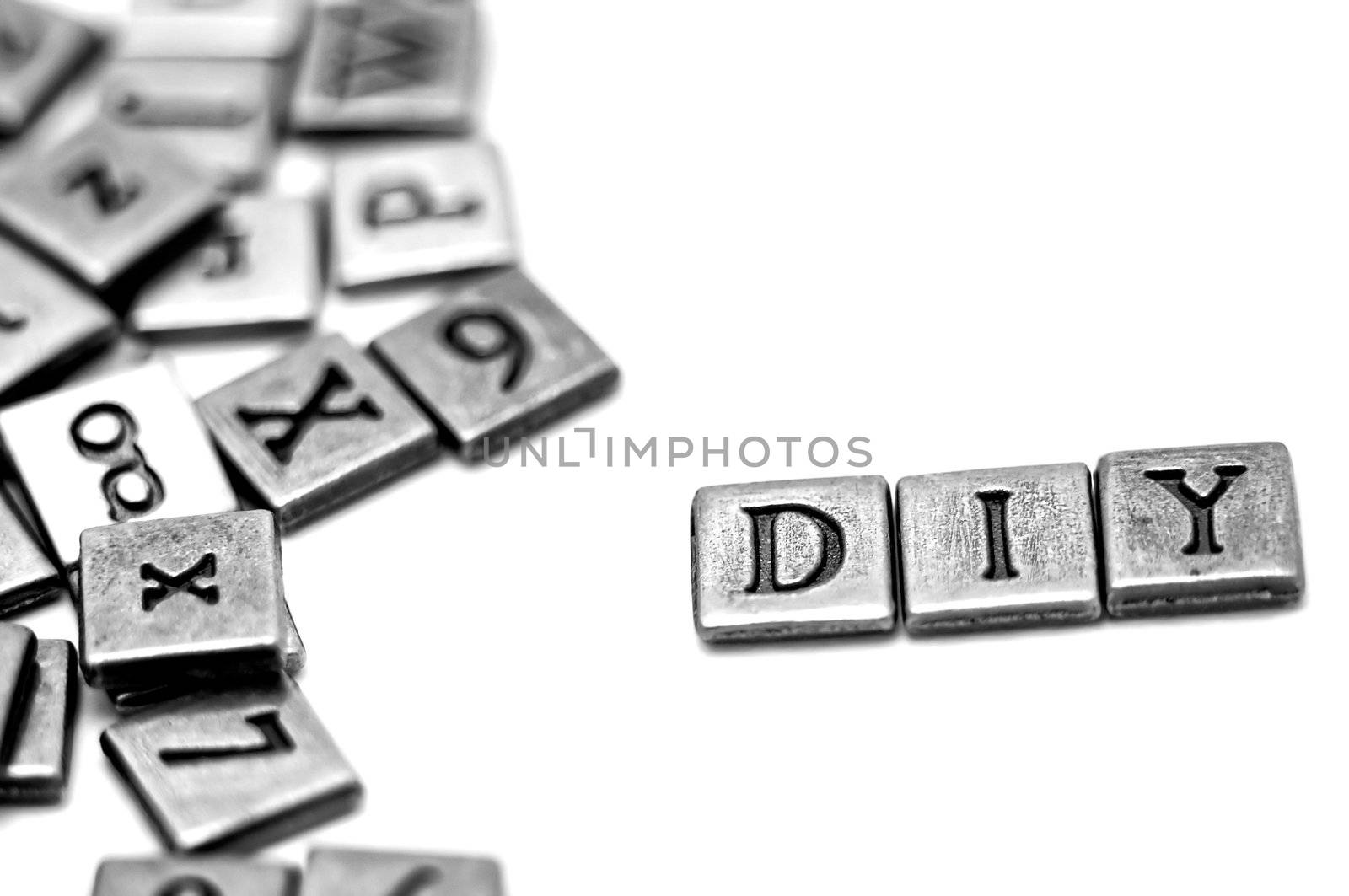 Metal scrapbooking letters spelling DIY: Do It Yourself. They lay on a white background and there is a bunch of other letters laying by.