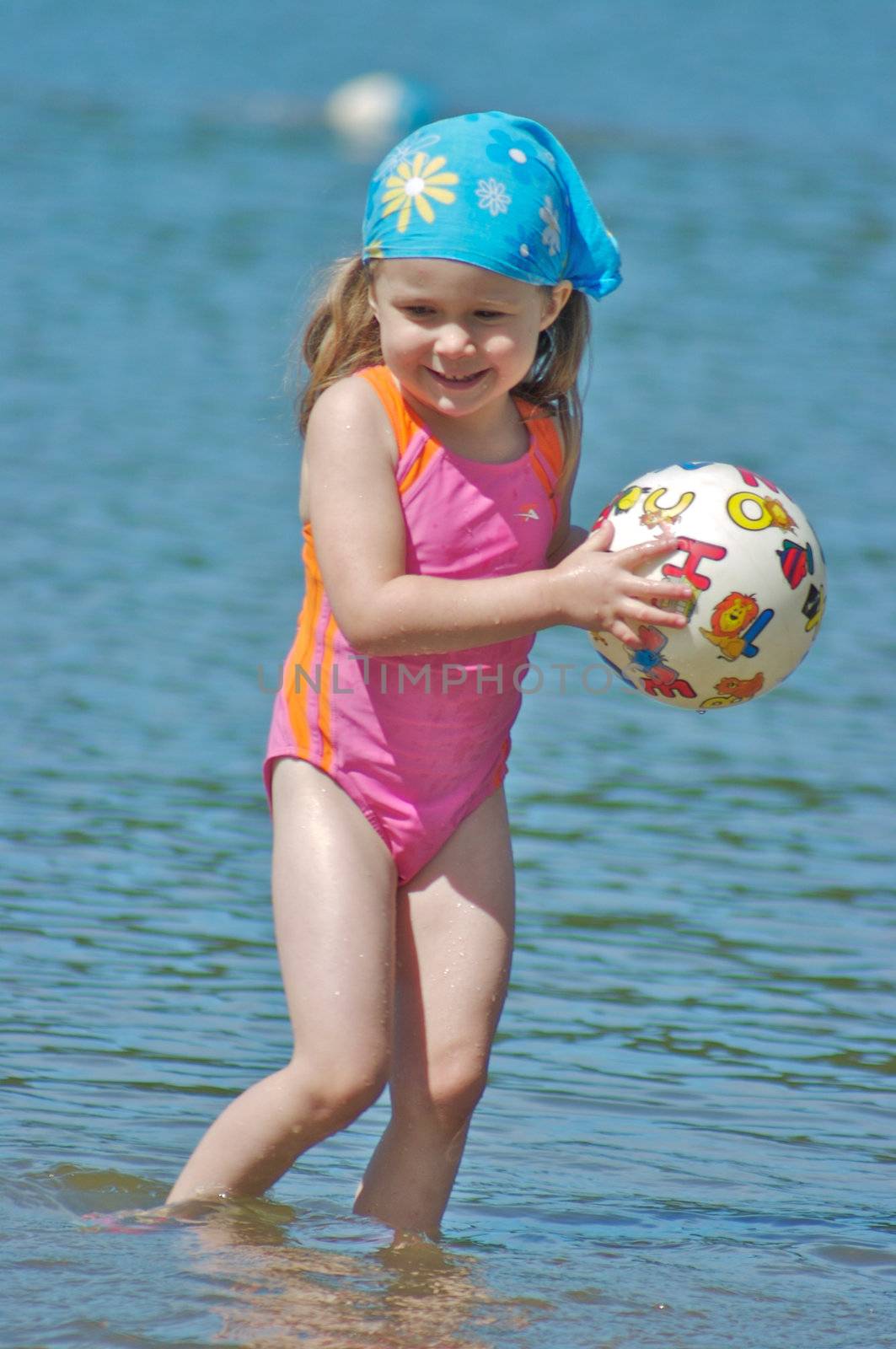 Cute little girl playing with a ball in the water