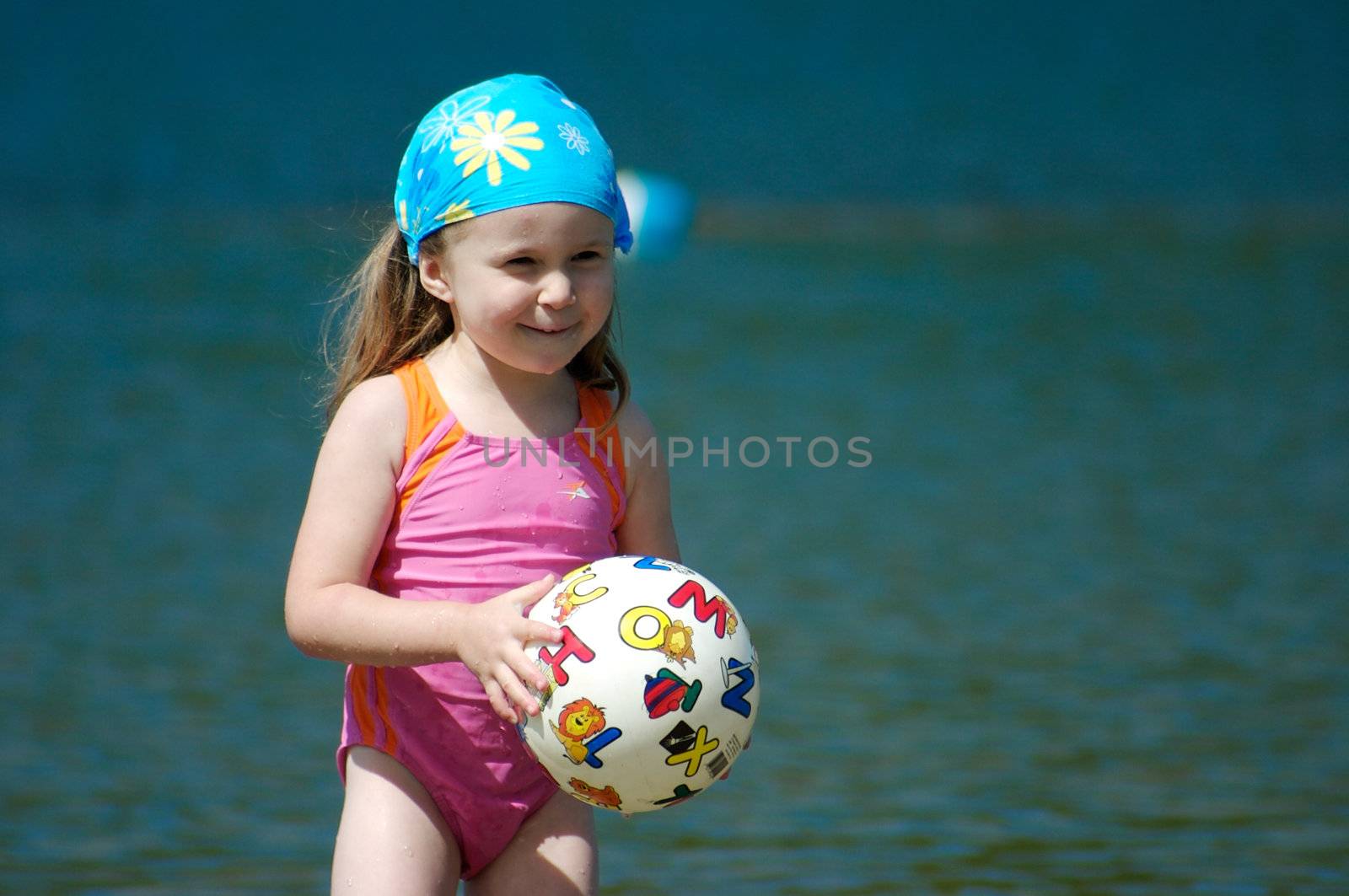 Cute little girl playing with a ball in the water