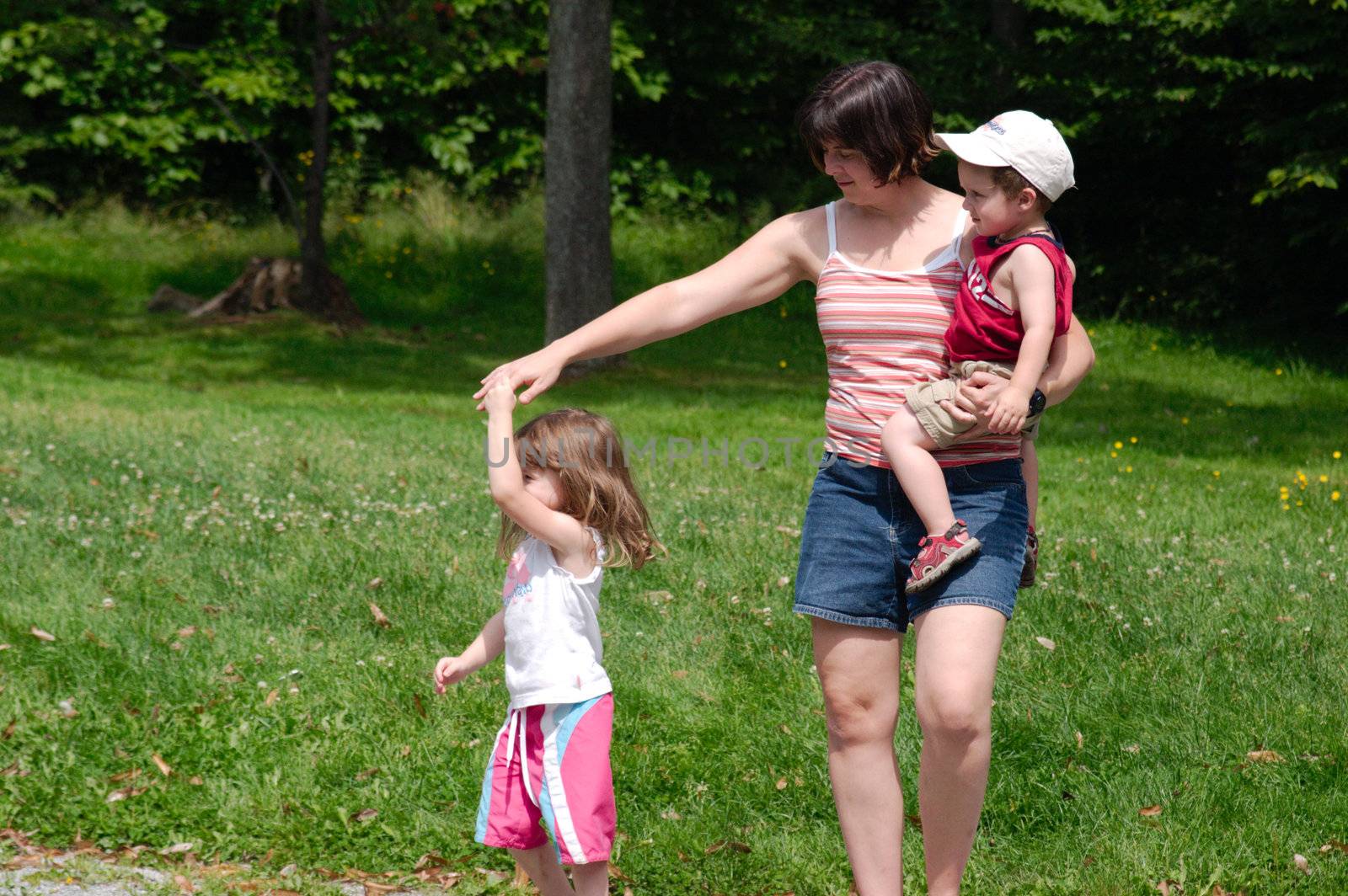 Happy familly (mother with 2 kids) walking in a park with the little daughter dancing