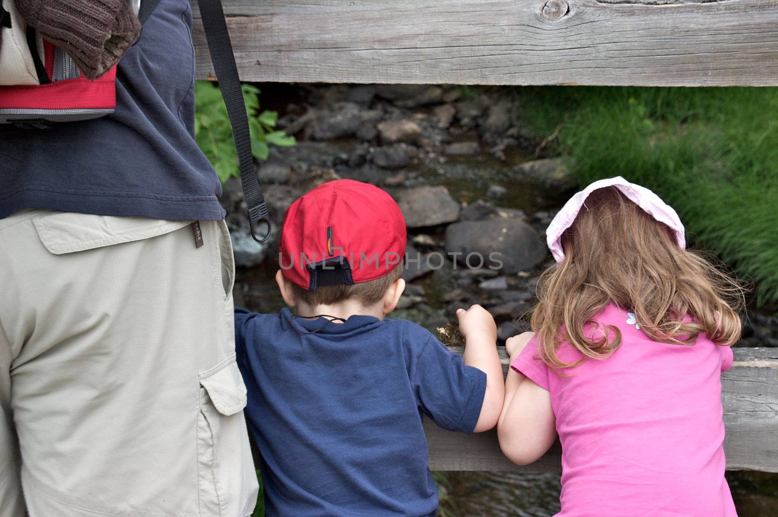 Family (father, daughter and son) standing on a bridge and looking down at a small river