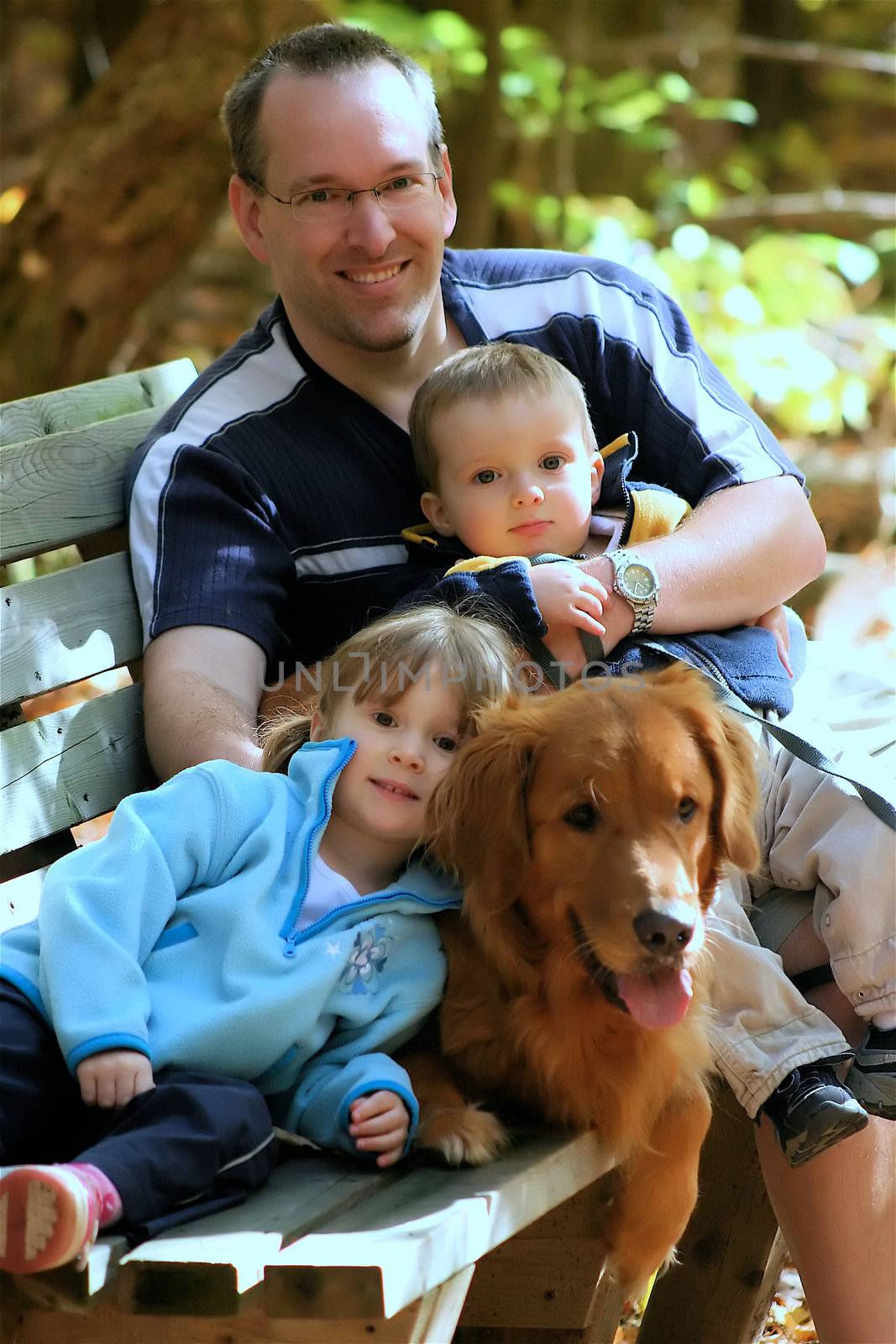 Happy family siting on a bench with their dog in autumn