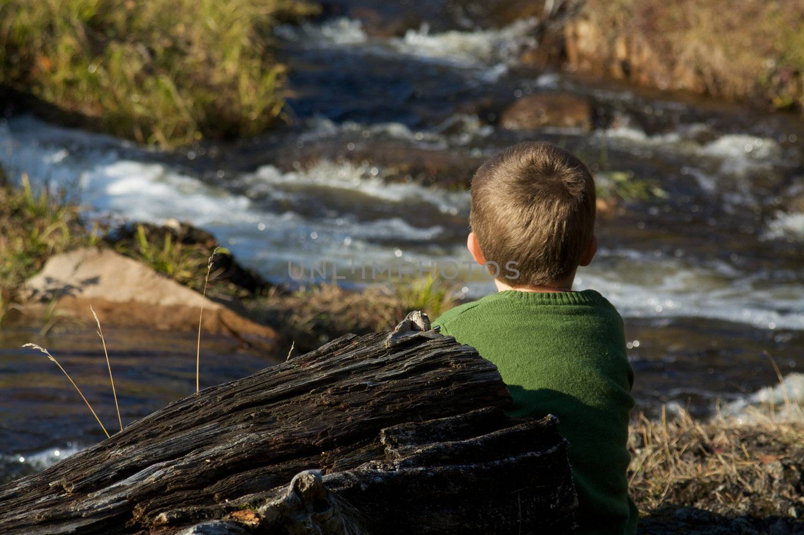 Cute little boy sitting by a river