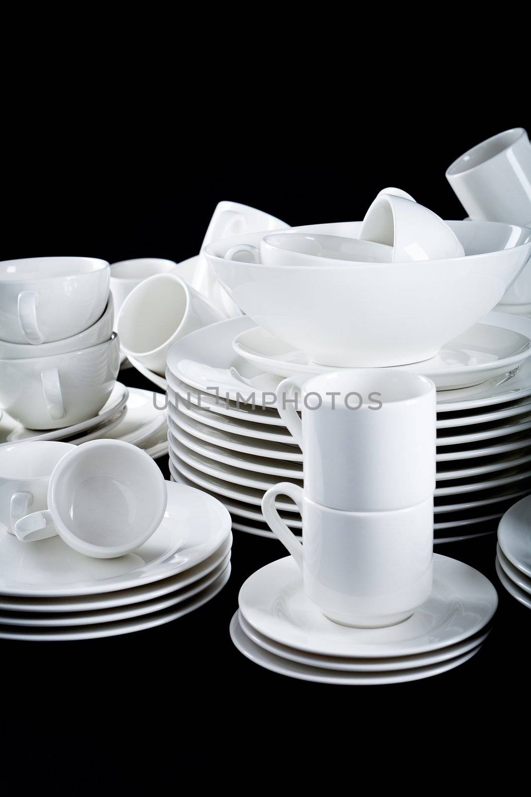 stack of mixed white dishes cups and plates isolated on black background