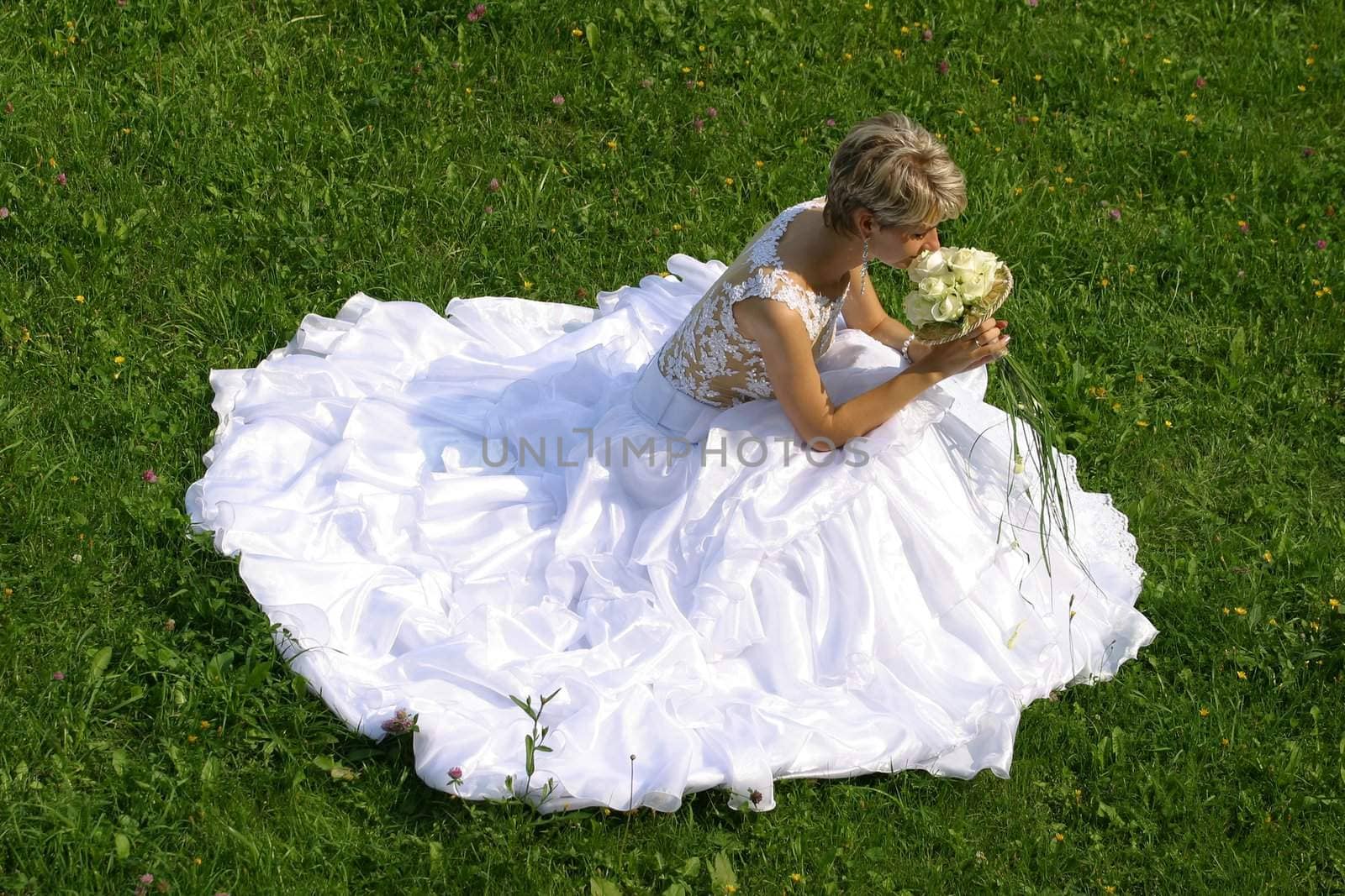 The beautiful bride with a wedding bouquet sits on a grass