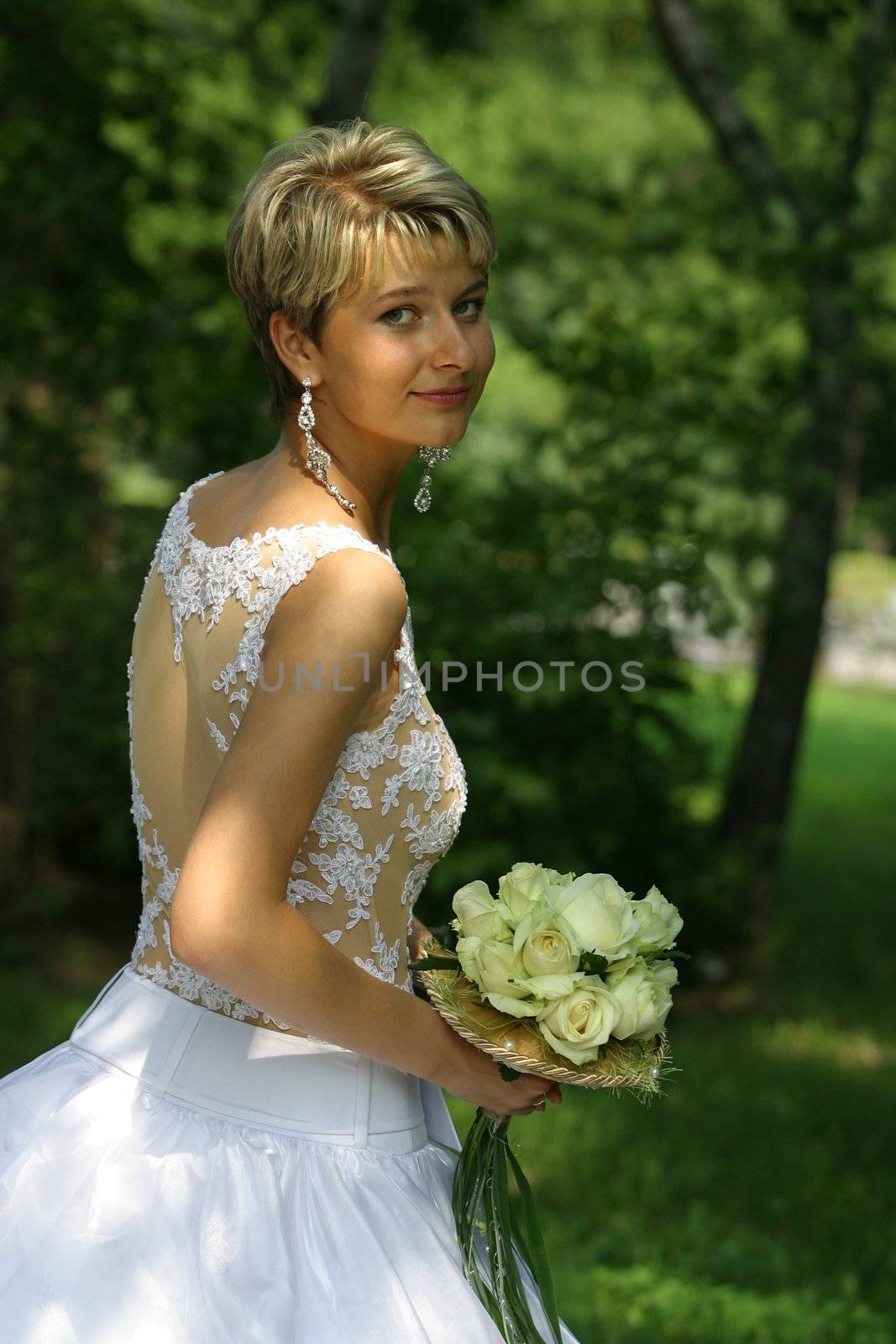 The beautiful bride in park with a wedding bouquet in hands