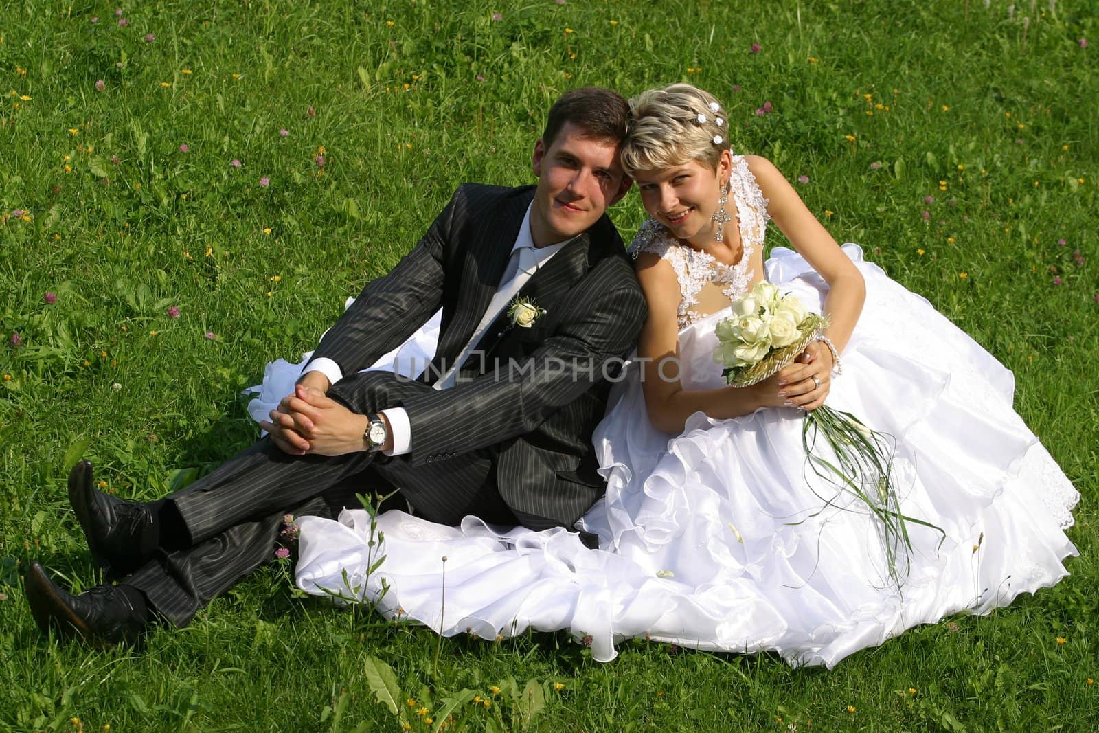 Beautiful newly-married couple sit on a grass