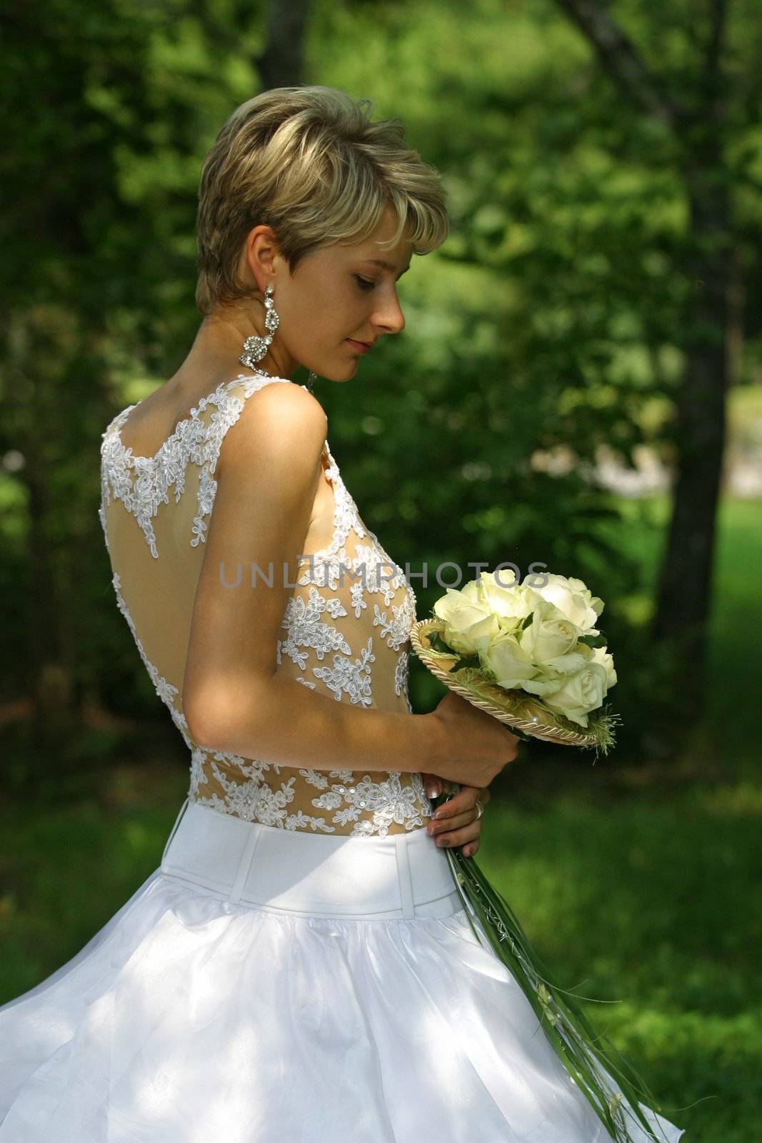 The beautiful bride in park with a wedding bouquet in hands