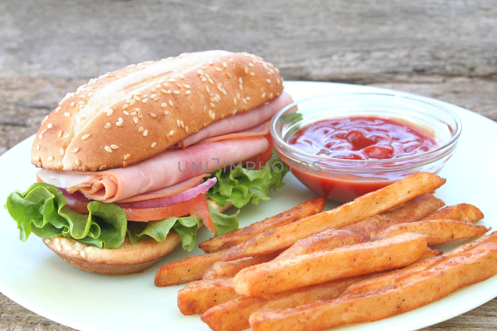 Ham hogie with the fixings and frech fries with ketchup on the side.