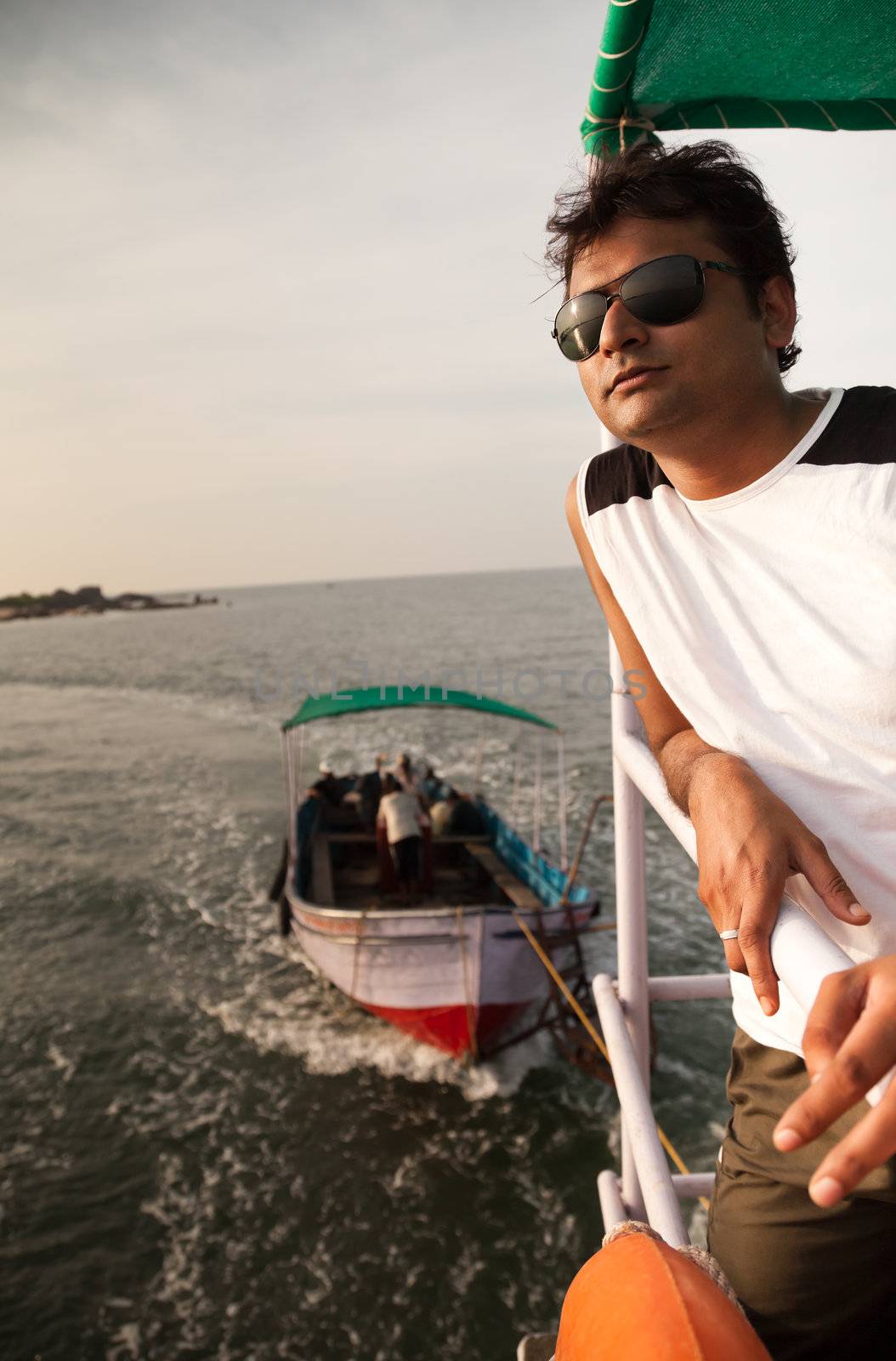 Indian Happy young man standing on boat in ocean with sunglasses