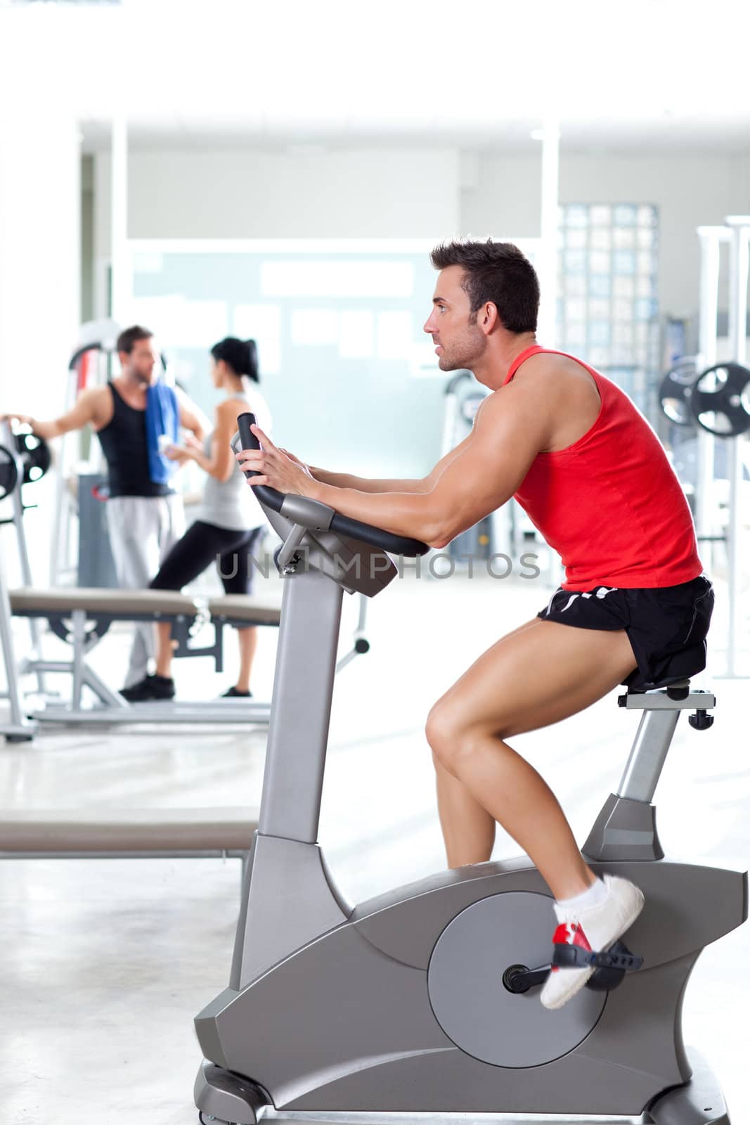 man on stationary bicycle at sport fitness gym interior