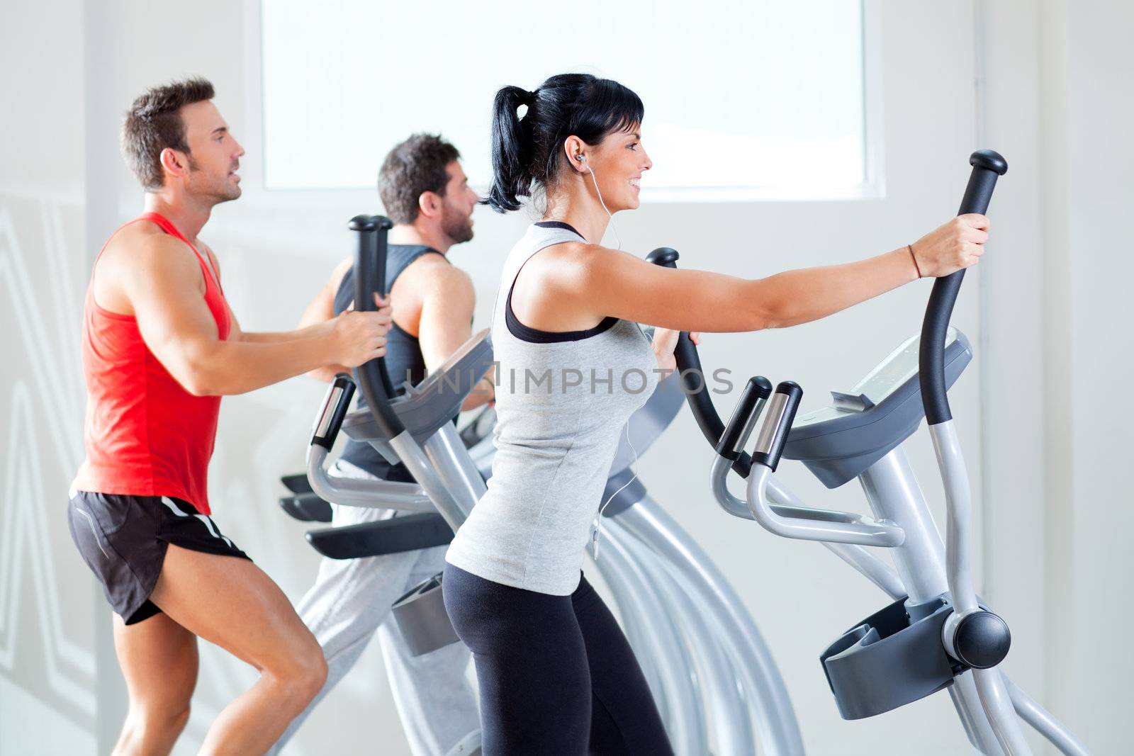 man and woman with elliptical cross trainer at gym by lunamarina