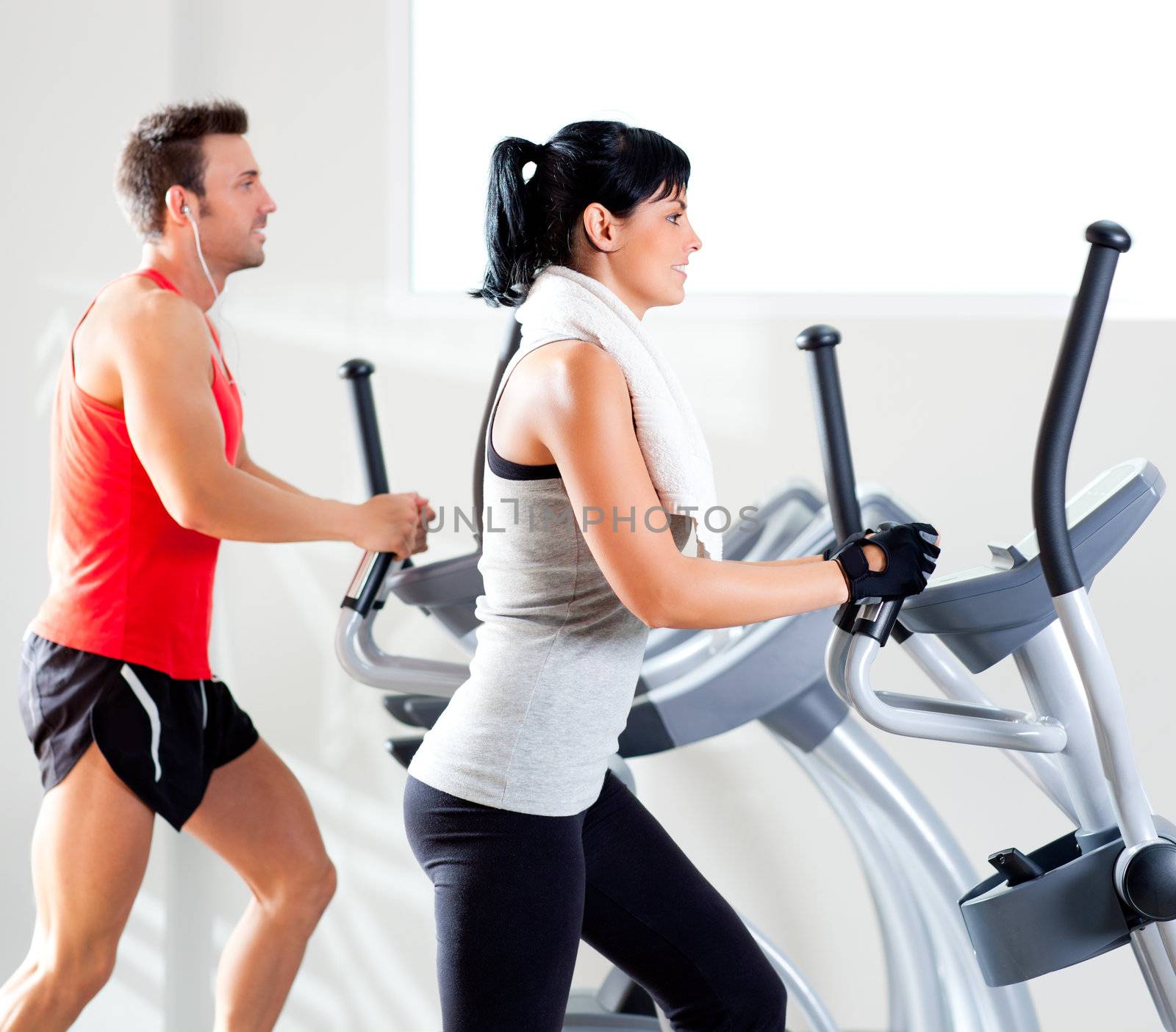 man and woman with elliptical cross trainer at gym by lunamarina