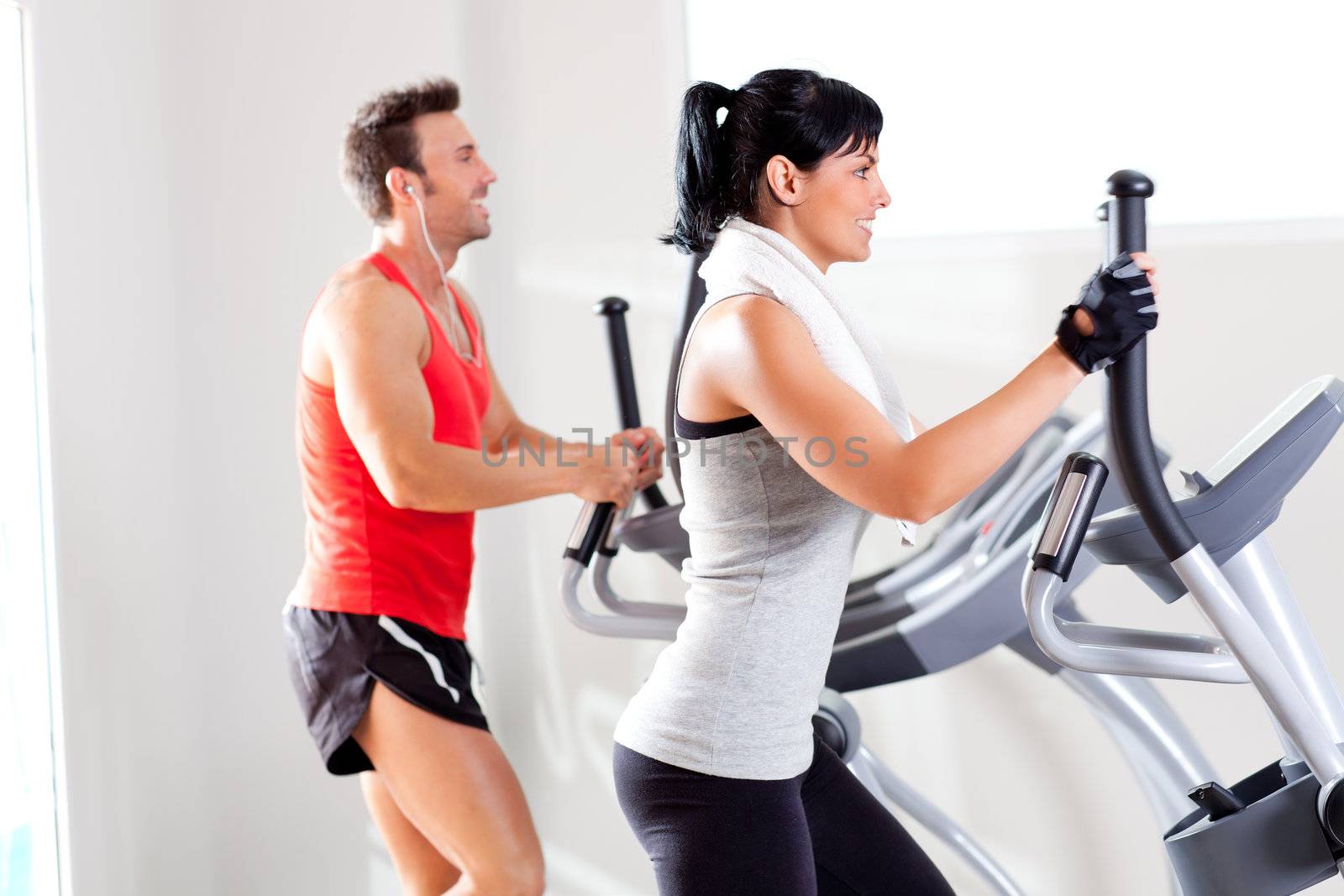 man and woman with elliptical cross trainer at gym by lunamarina