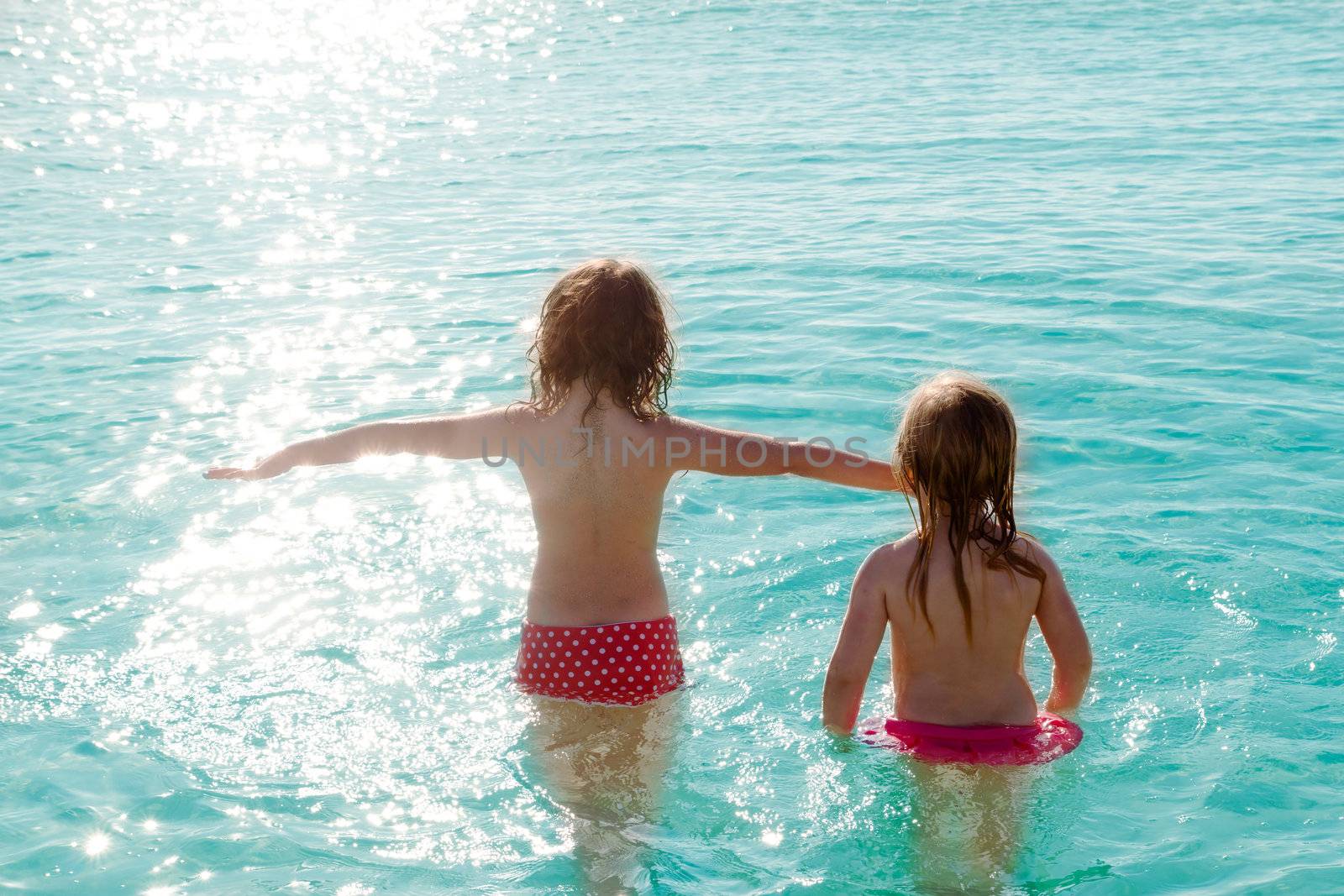 children girls rear view in the beach looking at sunset