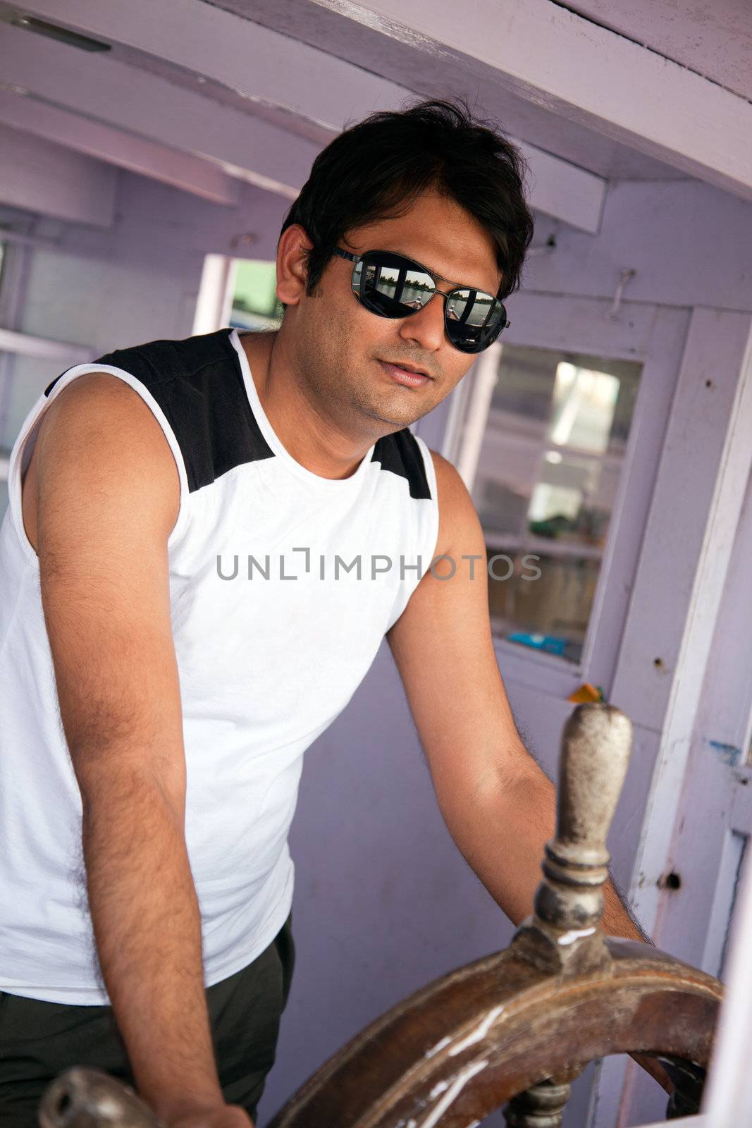 Indian Happy young man standing on boat in ocean with sunglasses