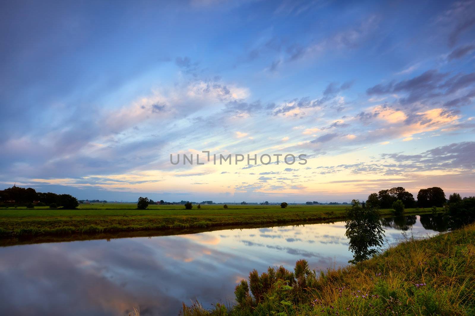 dramatic cloudscape over calm river at summer sunrise