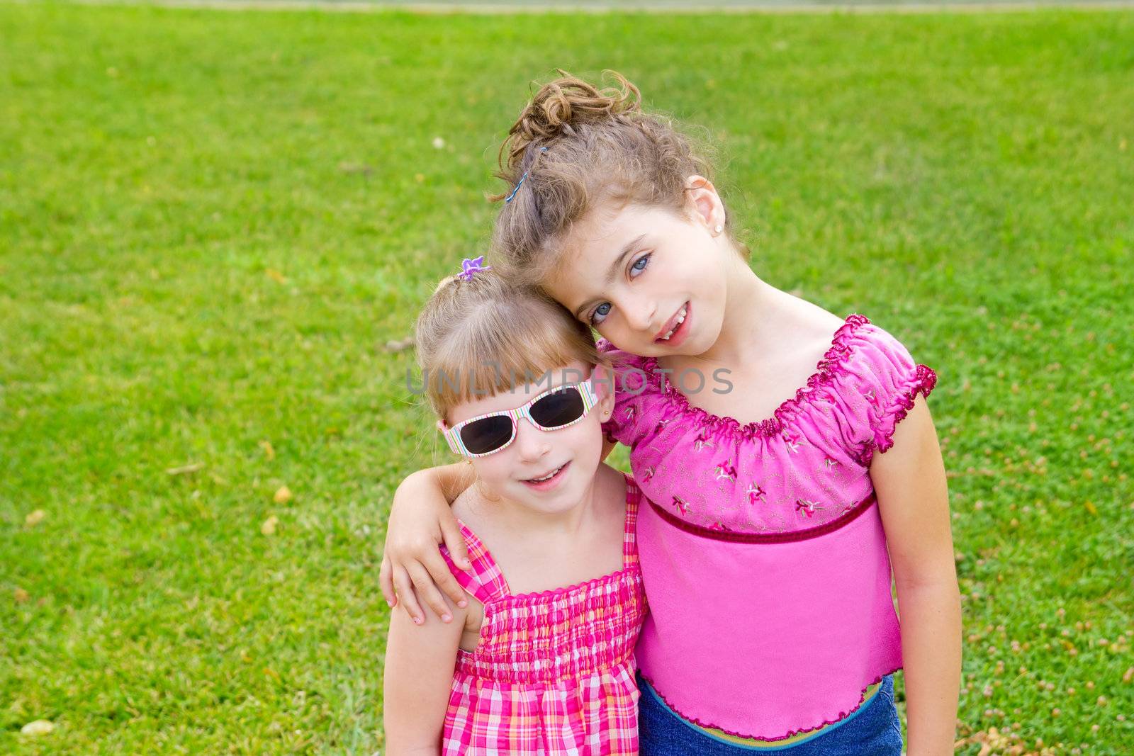 children girls hug in green grass park with pink dress