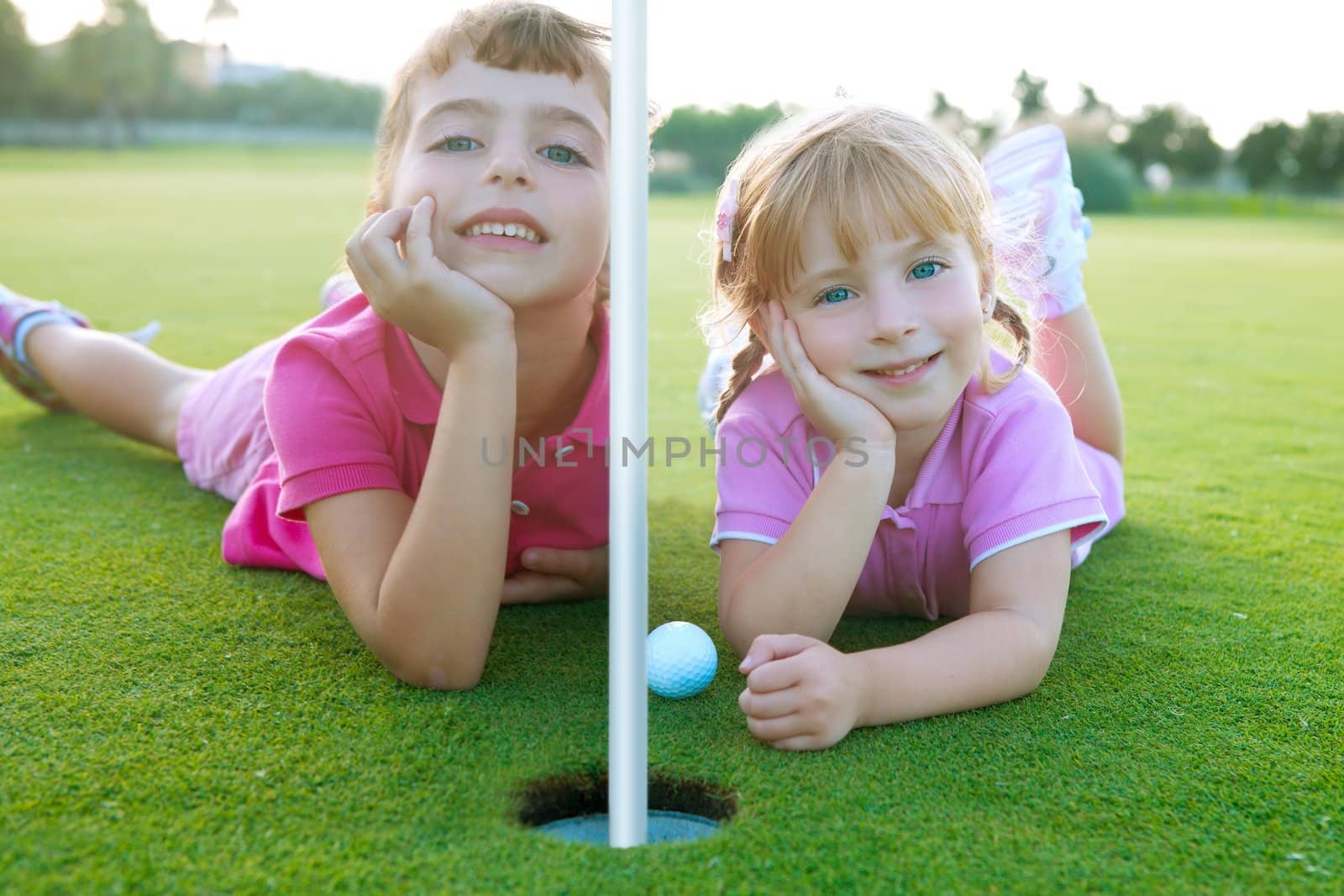 Golf two sister girls relaxed lying near green hole with ball