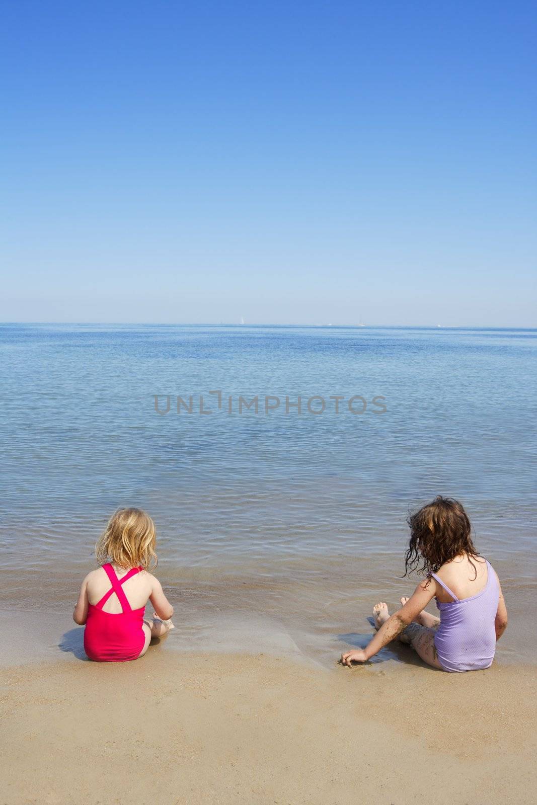 tow sisters sit on beach bathing suit swimsuit back view summer vacation