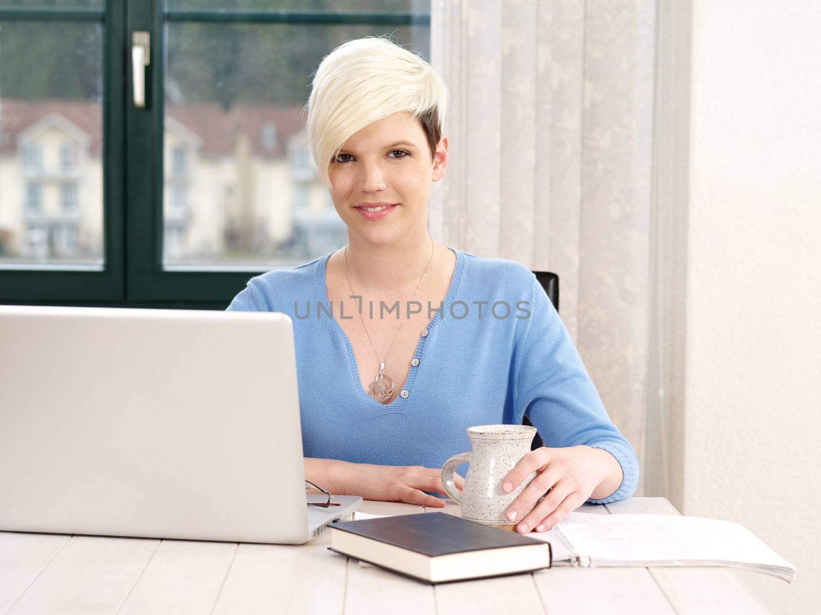 Photo of a beautiful blond female working in an office on a laptop and writing in a notebook.
