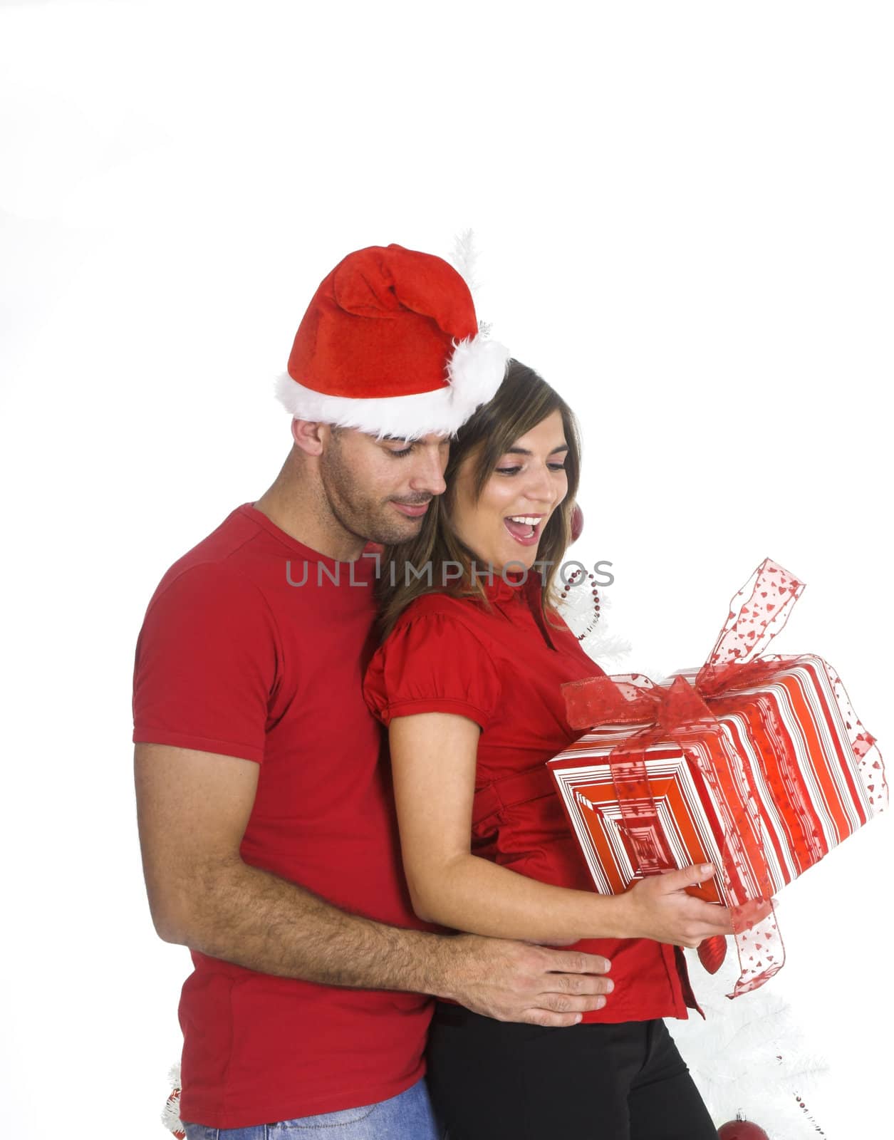 Happy couple holding a Christmas present near a white tree