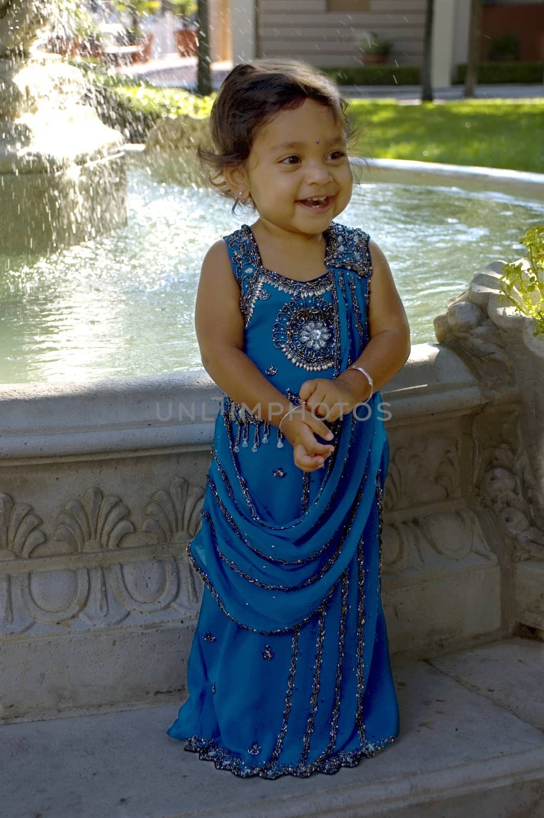A little Indian girl in her sari standing at the fountain.