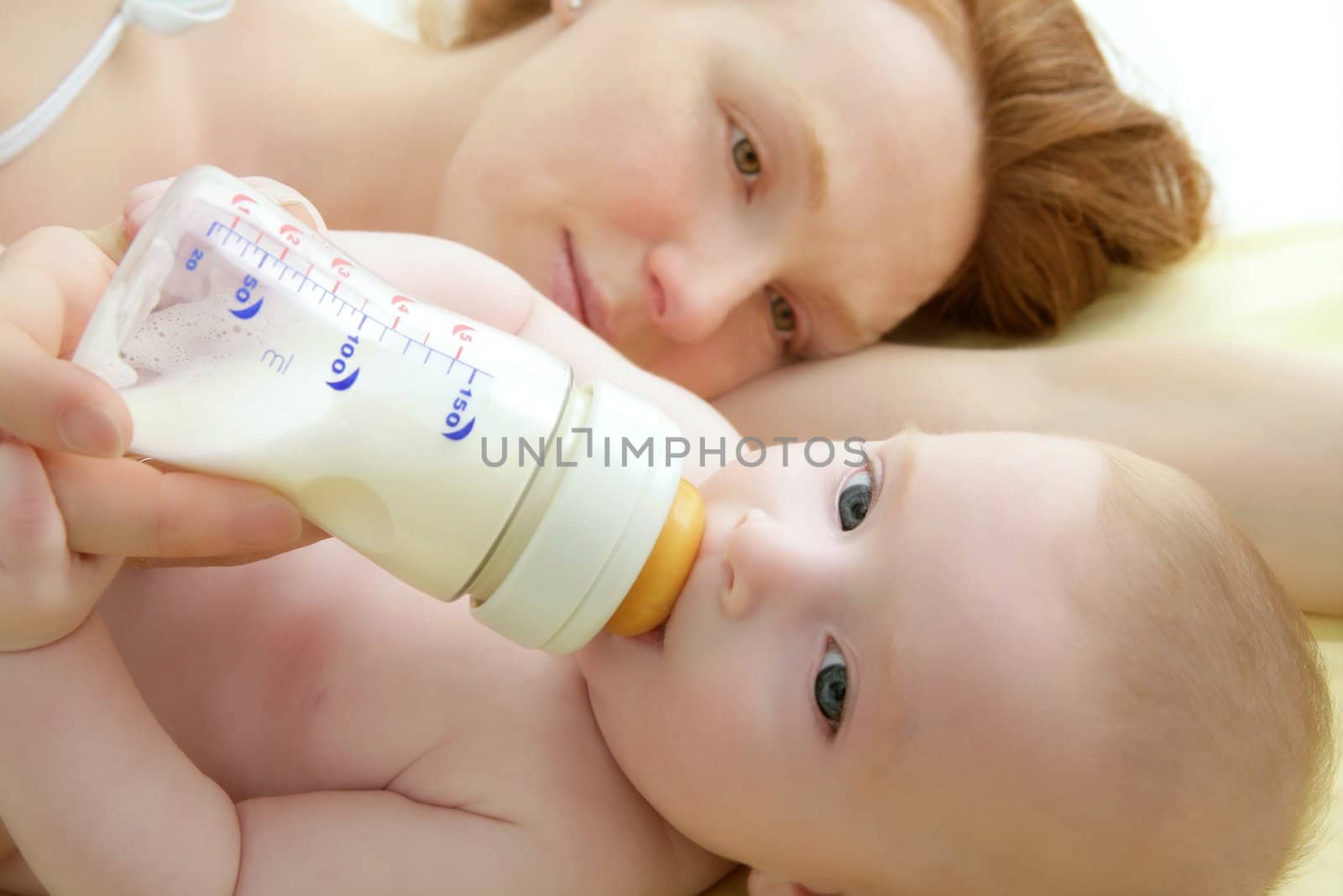 baby blond drinking bottle from mother hands