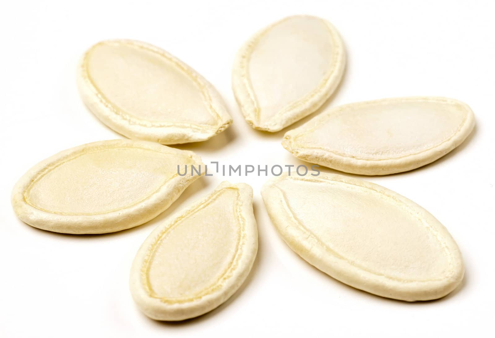 Pumpkin seeds arranged in flower shape on white background.