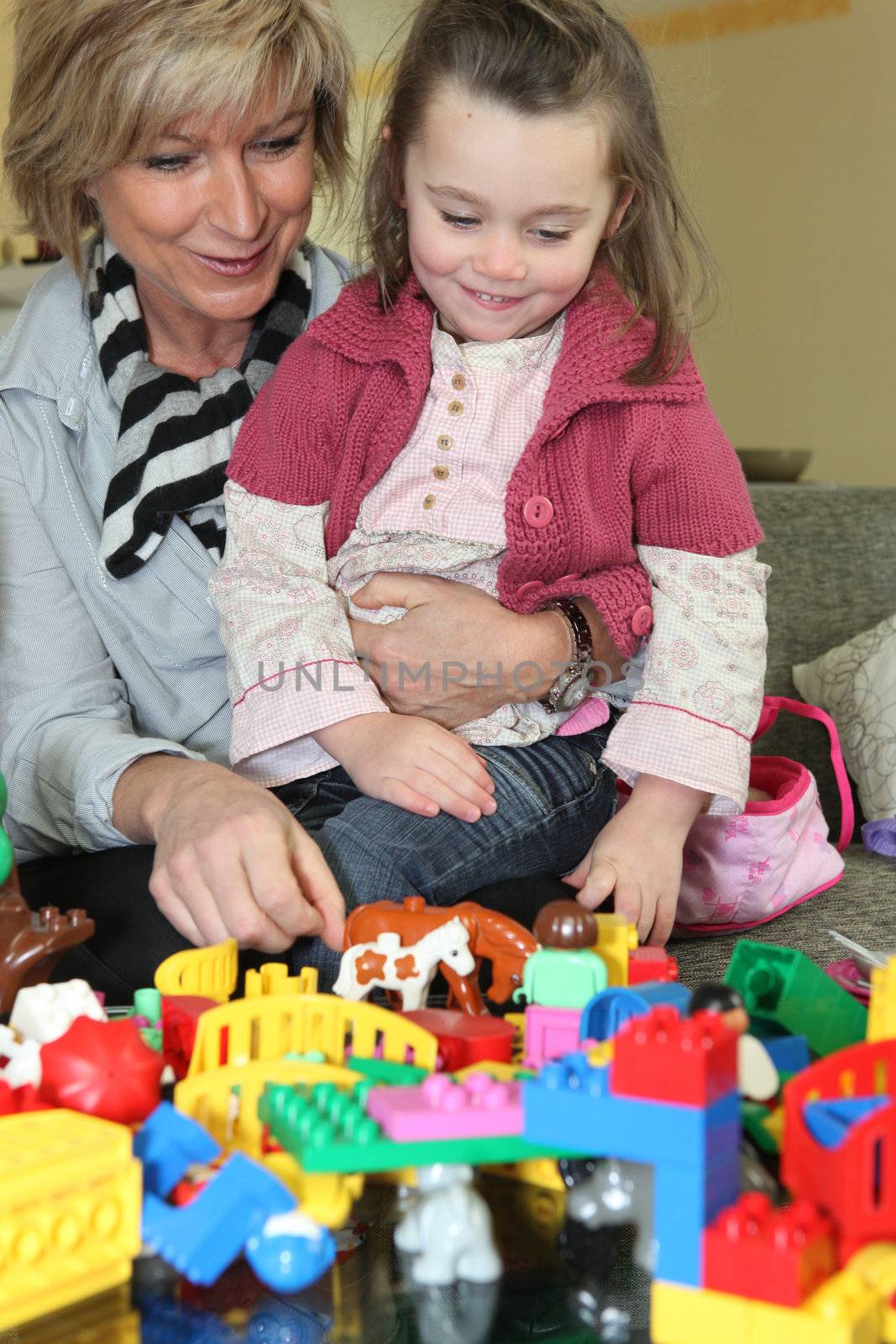 Mother and daughter playing with toys at home by phovoir