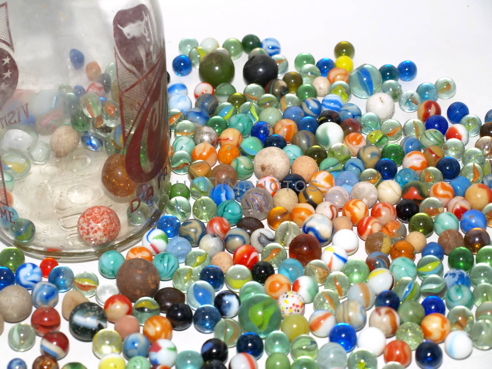 An assortment of various marbles and shooters spilled out next to a glass bottle.