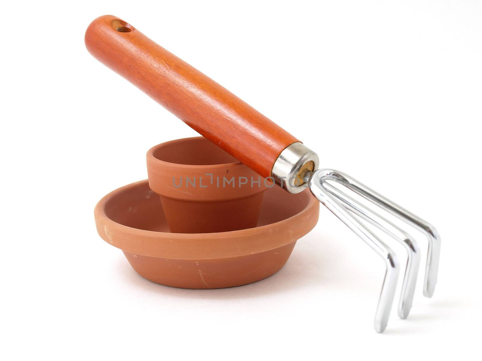 Gardening tool and terra cotta pot and saucer isolated against a white background.