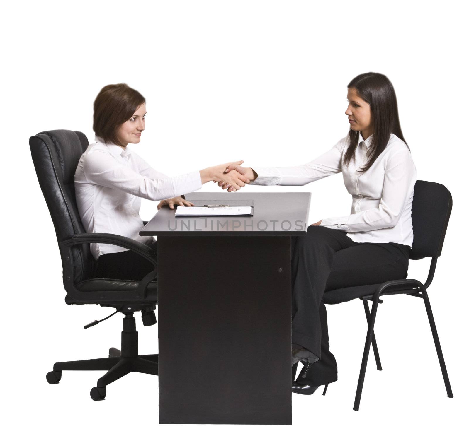 Two businesswomen shaking hands over the office desk.