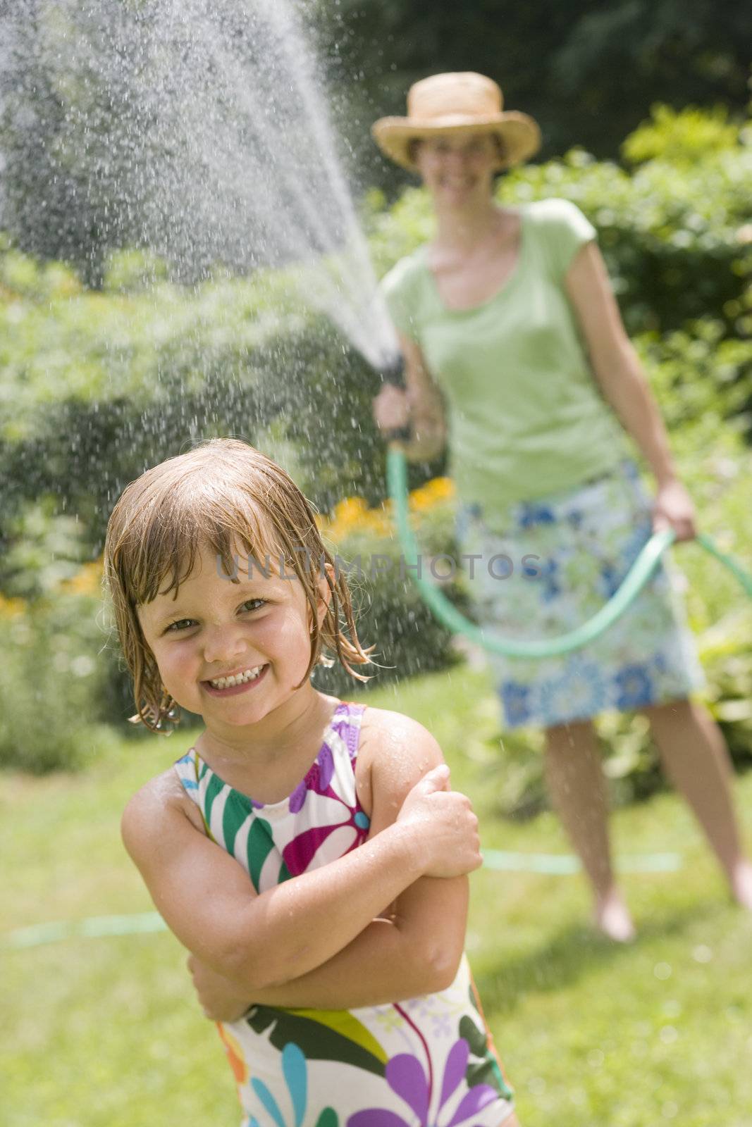 Pretty woman spraying little girl with water from a garden hose in the Summertime