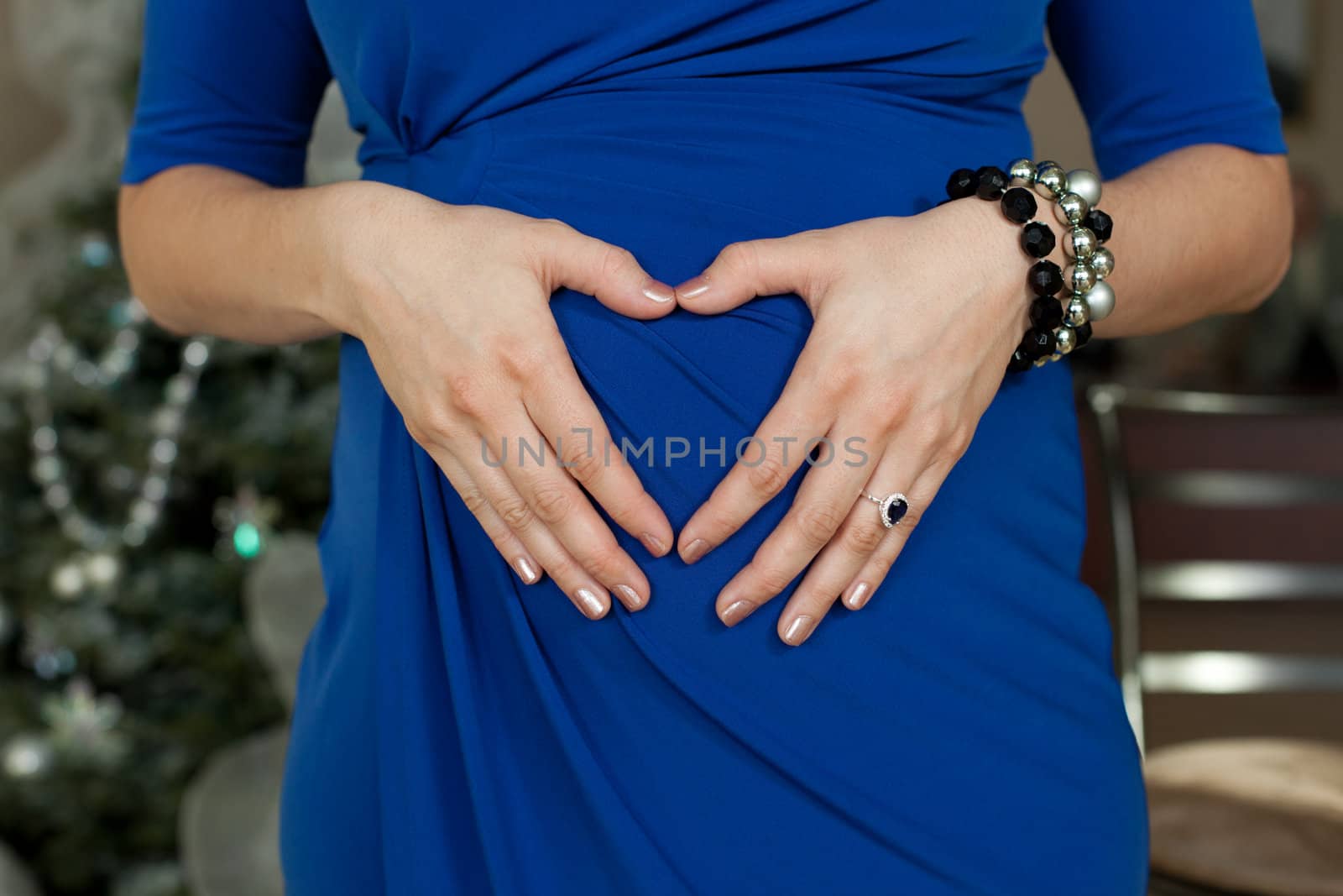 Young mother in blue dress making a heart shape with her hands against her belly.