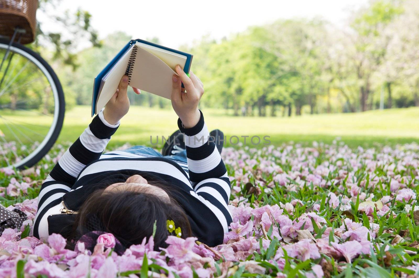 Asian woman reading booklet on the grass by Myimagine