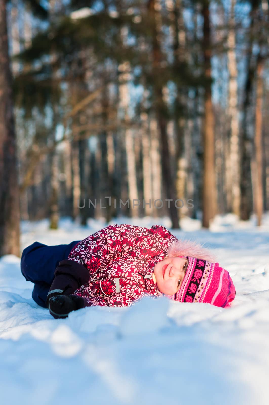 Baby lays on snow in wood, looks and smile