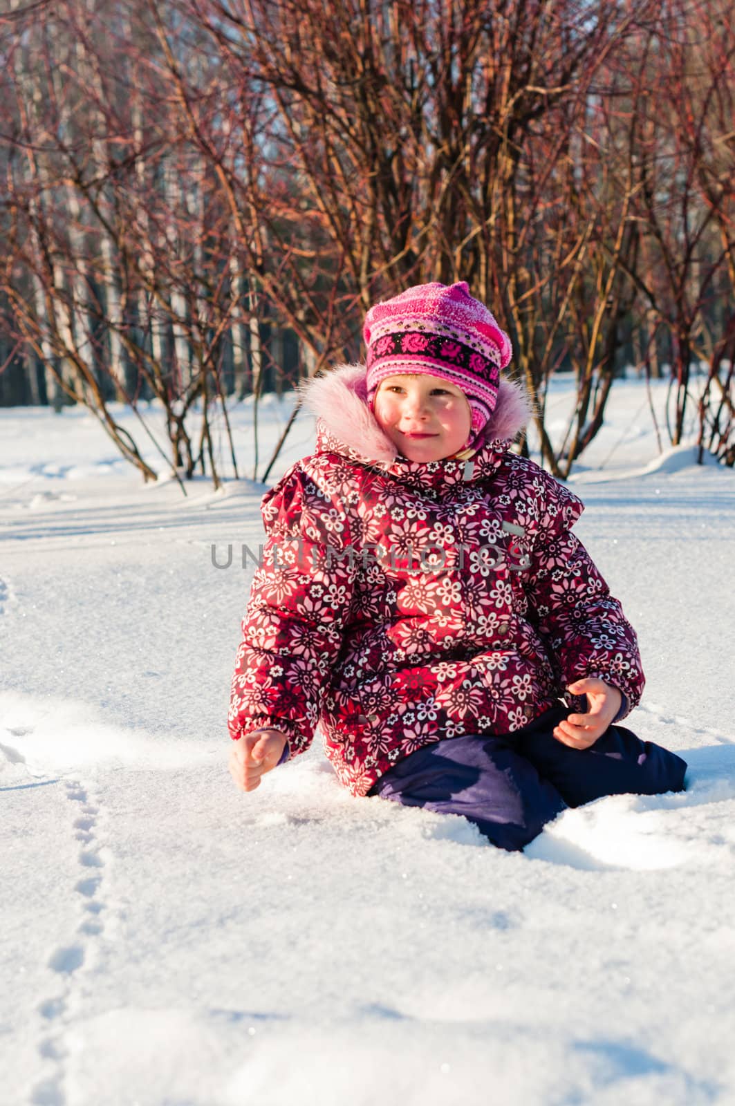 Baby sits on snow and looks on the left side