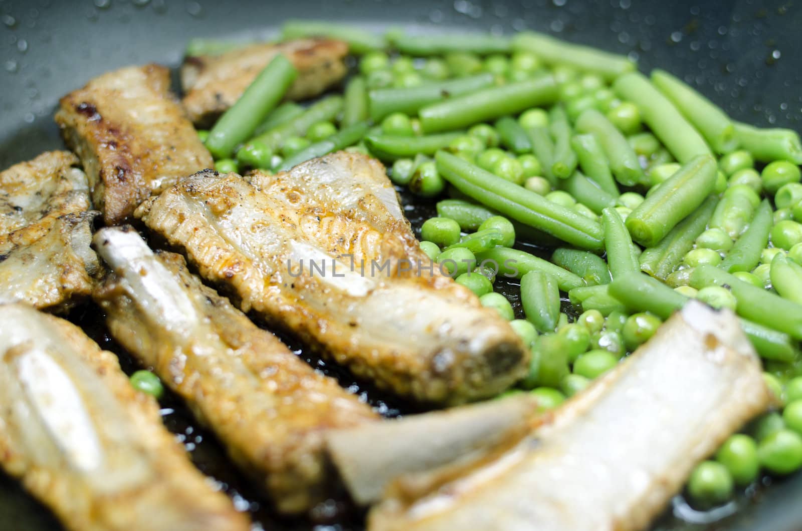 Pork ribs with peas and green beans prepared in a frying pan