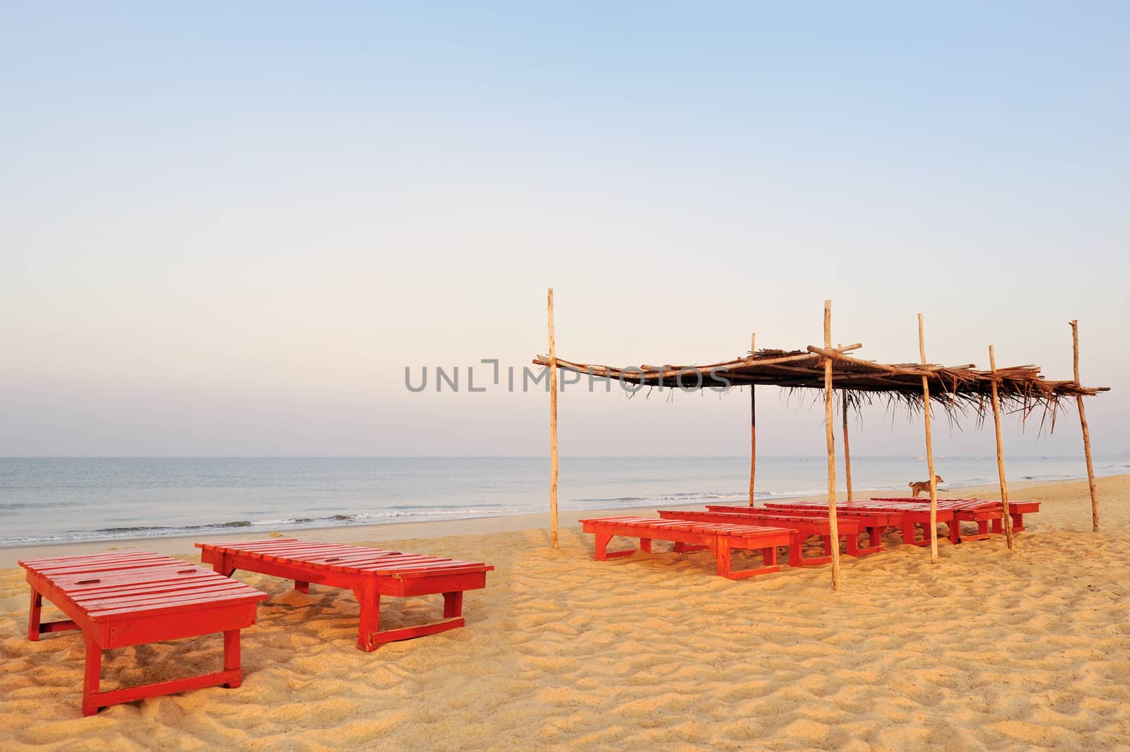 Exotic lean-tos of palm leaves and red deck-chairs on tropical beach
