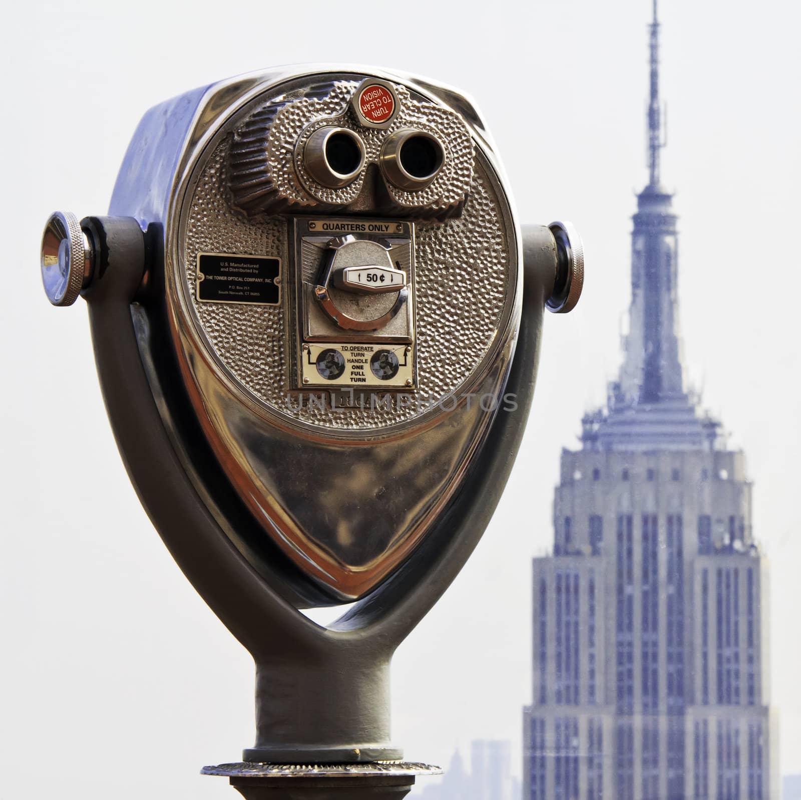 A close up of coin binoculars atop a New York City skyscraper with a bokeh Empire State Building in the background.
