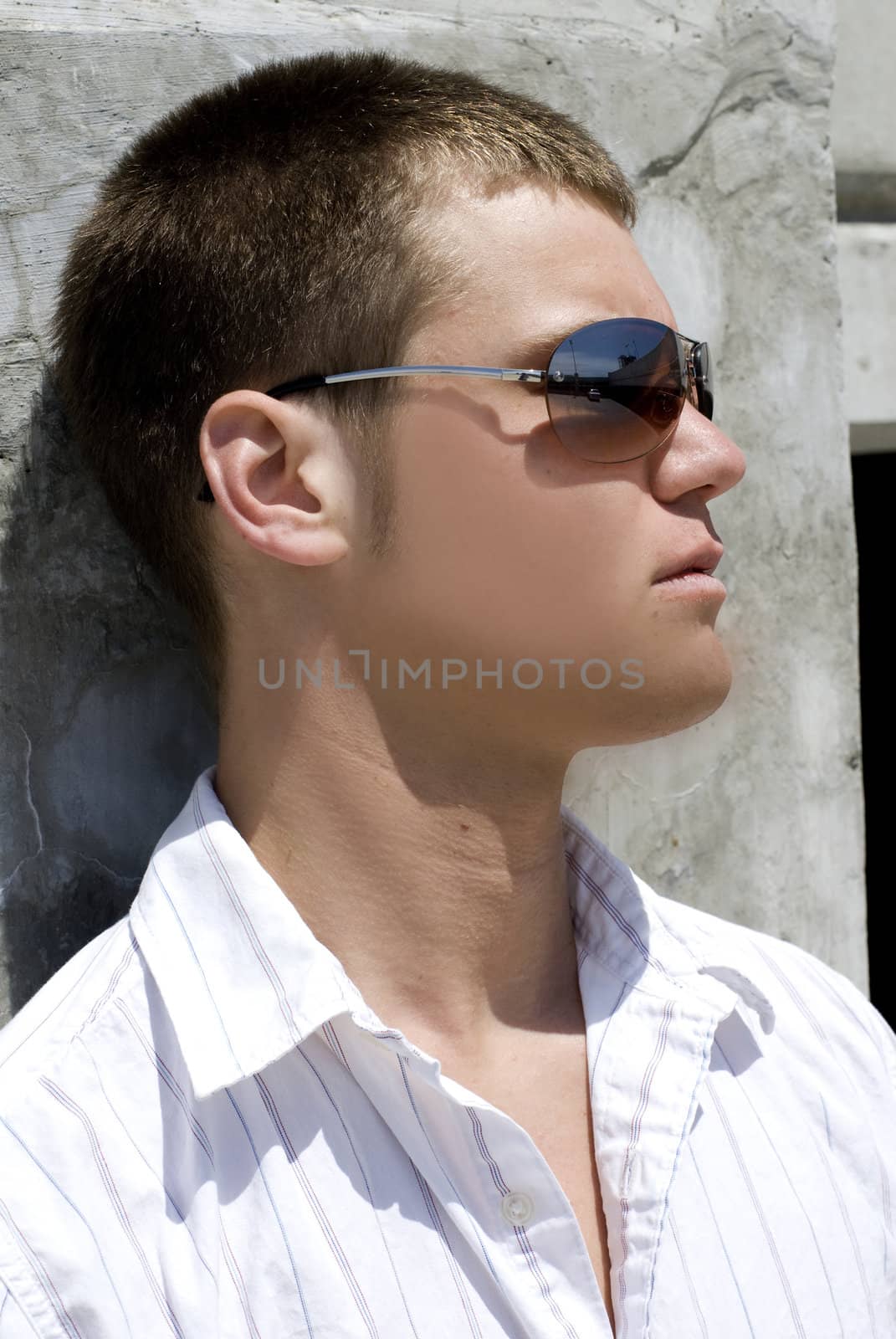 A young man outside against a wall.