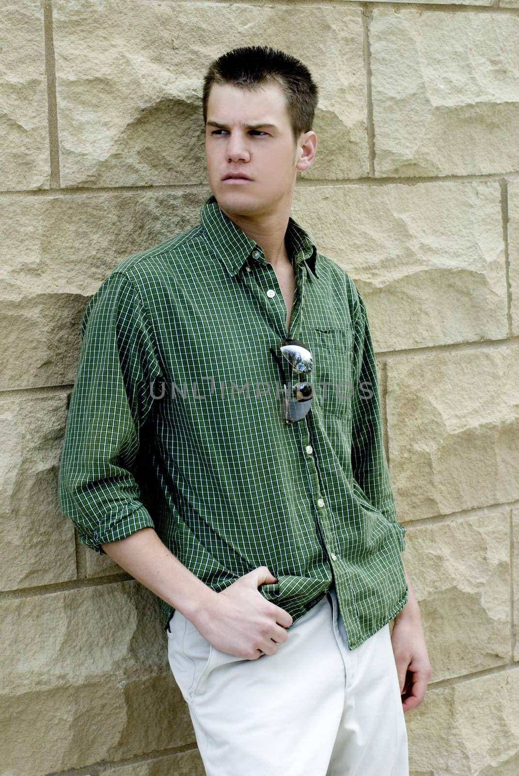 A young man outside against a wall.