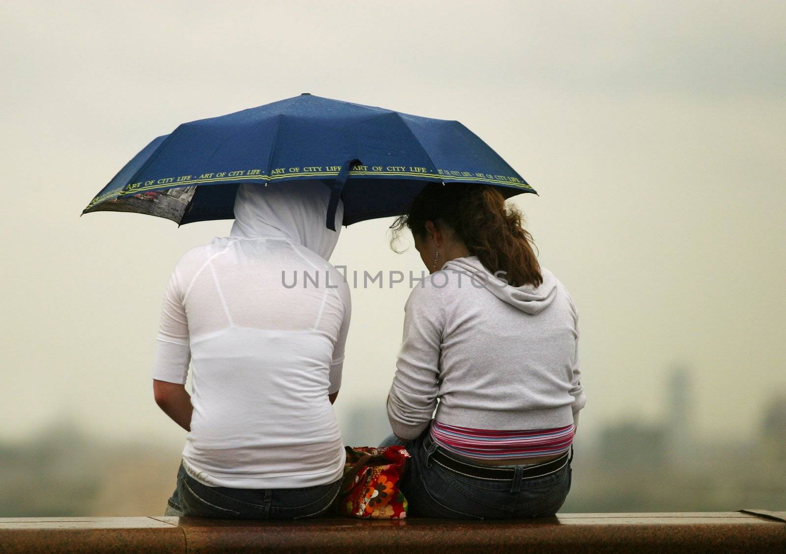 Two girls under dark blue umbrella on a background of the evening sky