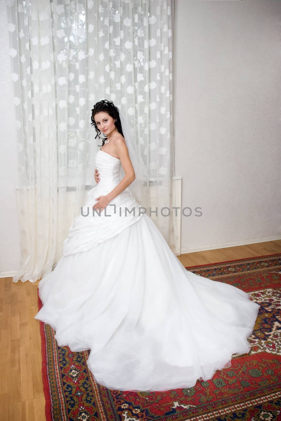 bride waits for her groom in her house, standing by the window