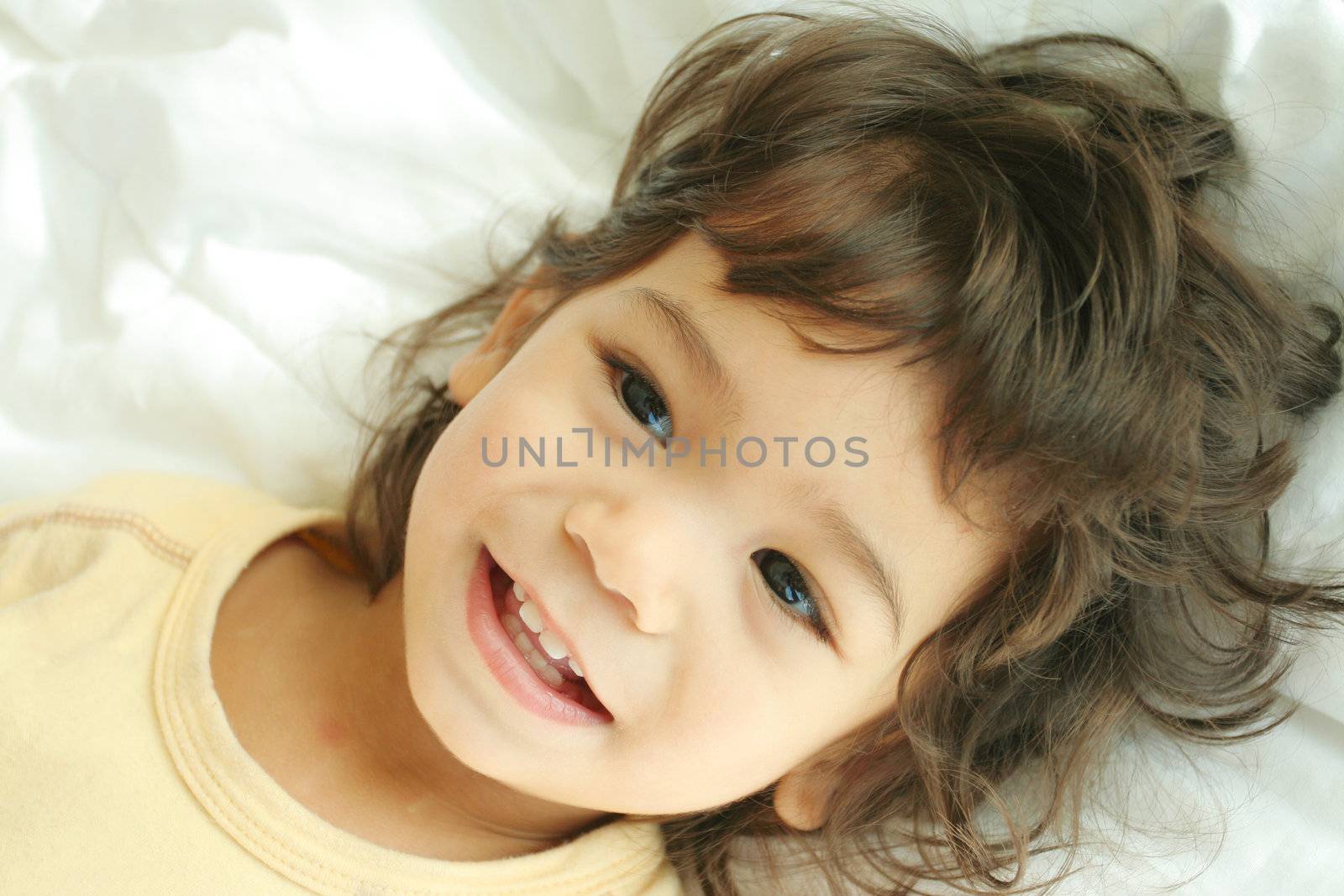 Beautiful toddler boy lying on bed laughing and smiling. Part asian, scandinavian descent.