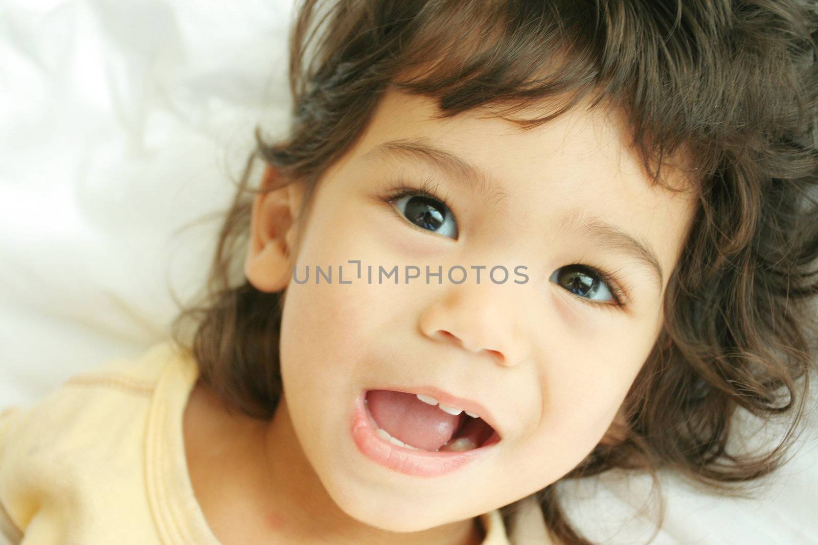 Beautiful toddler boy lying on bed laughing and smiling. Part asian, scandinavian descent.
