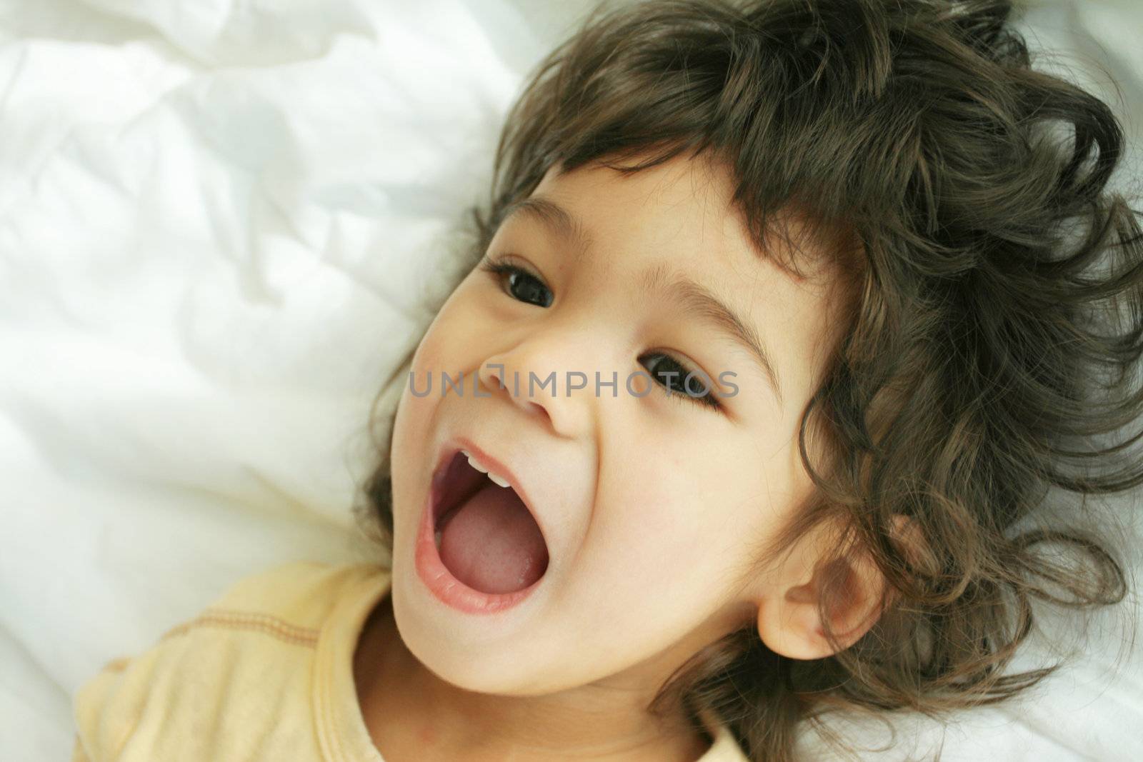 Beautiful toddler boy lying on bed laughing and smiling. Part asian, scandinavian descent.